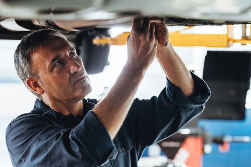 Mechanic inspecting the underside of a vehicle in a garage