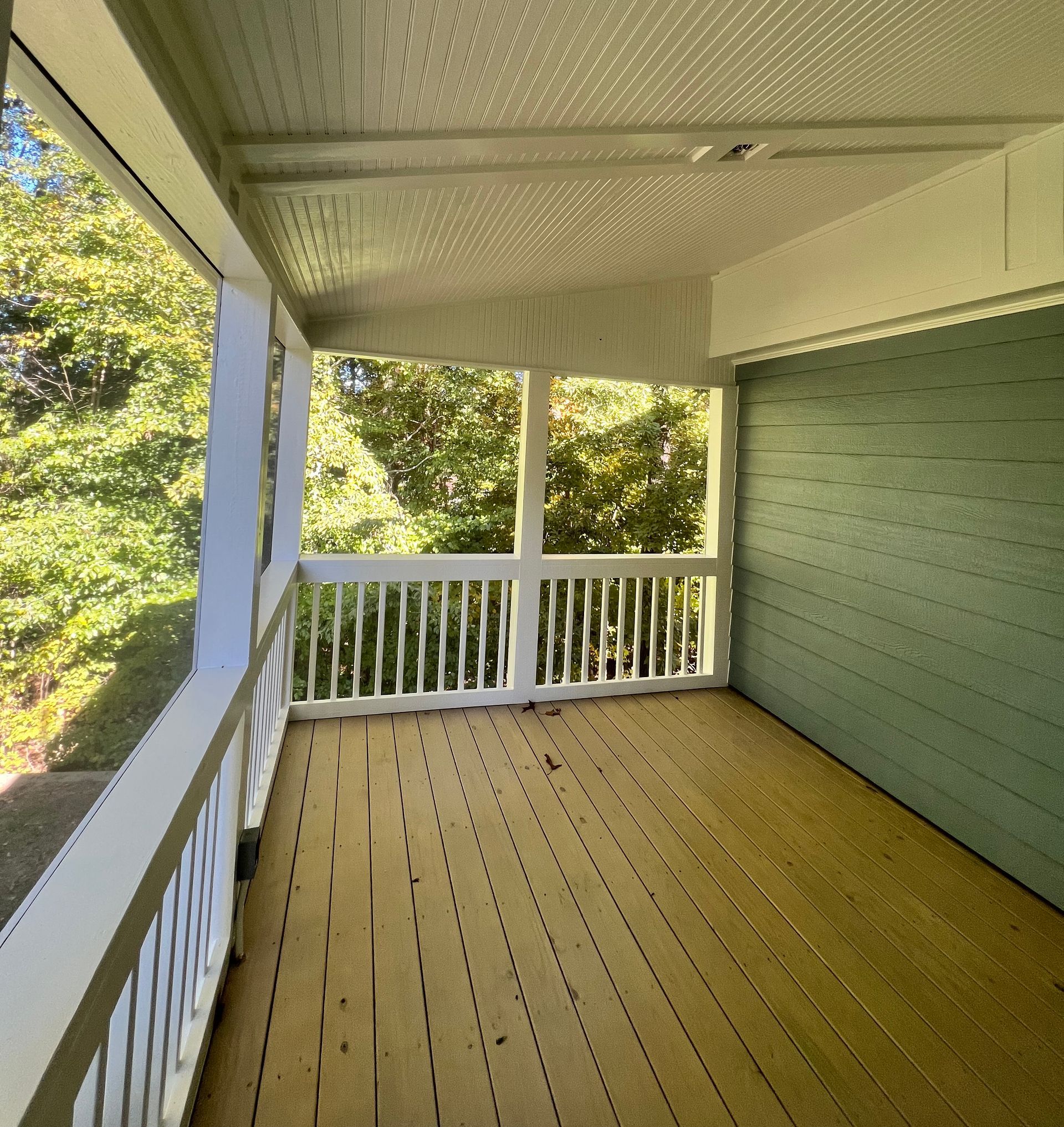 Screened porch with yellow floor, white railings, and green wall, overlooking trees.