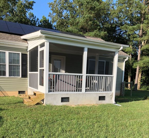 Screened-in porch on a green house with a white railing, concrete base, and stairs. Green grass in the foreground.