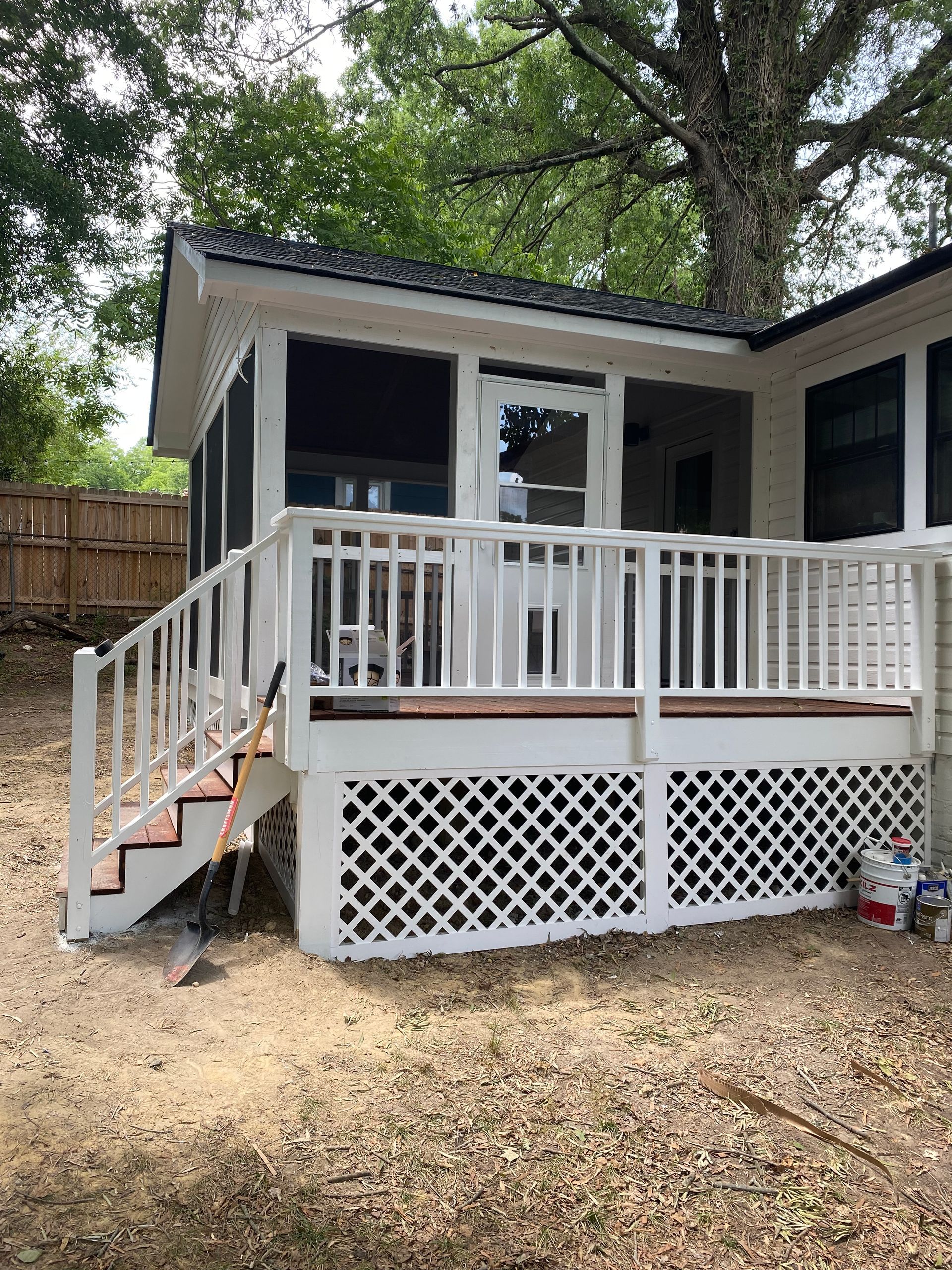 White screened-in porch with a deck, steps, and latticework skirting in a backyard.