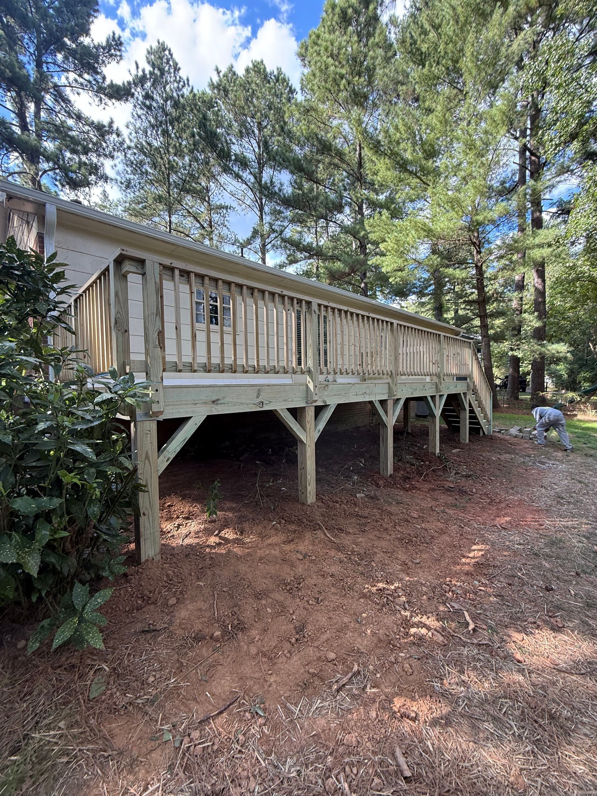 Wooden deck on a raised foundation, set against a backdrop of trees.