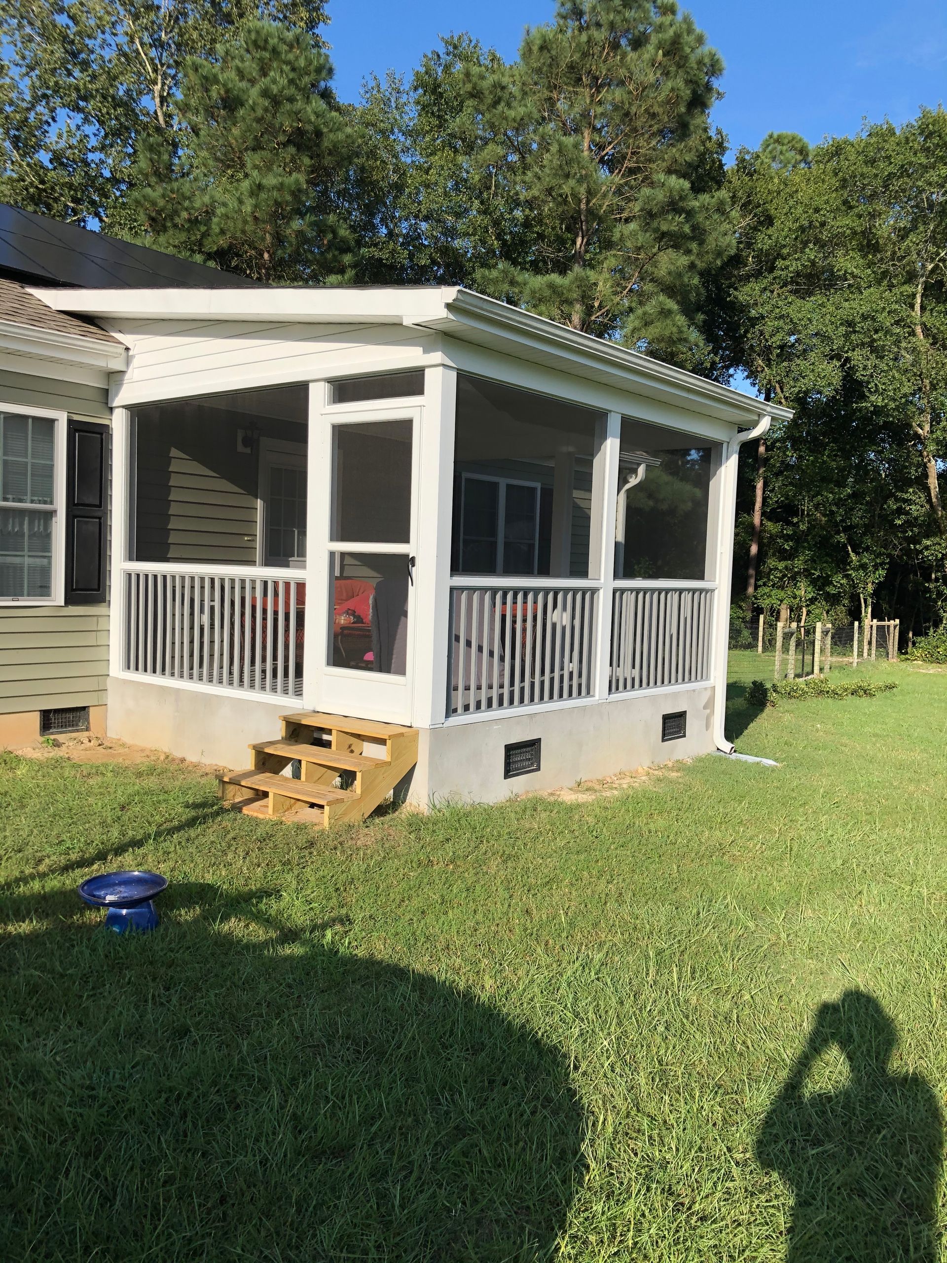 Screened porch with white railings and steps, attached to a house with green siding, on a grassy yard.