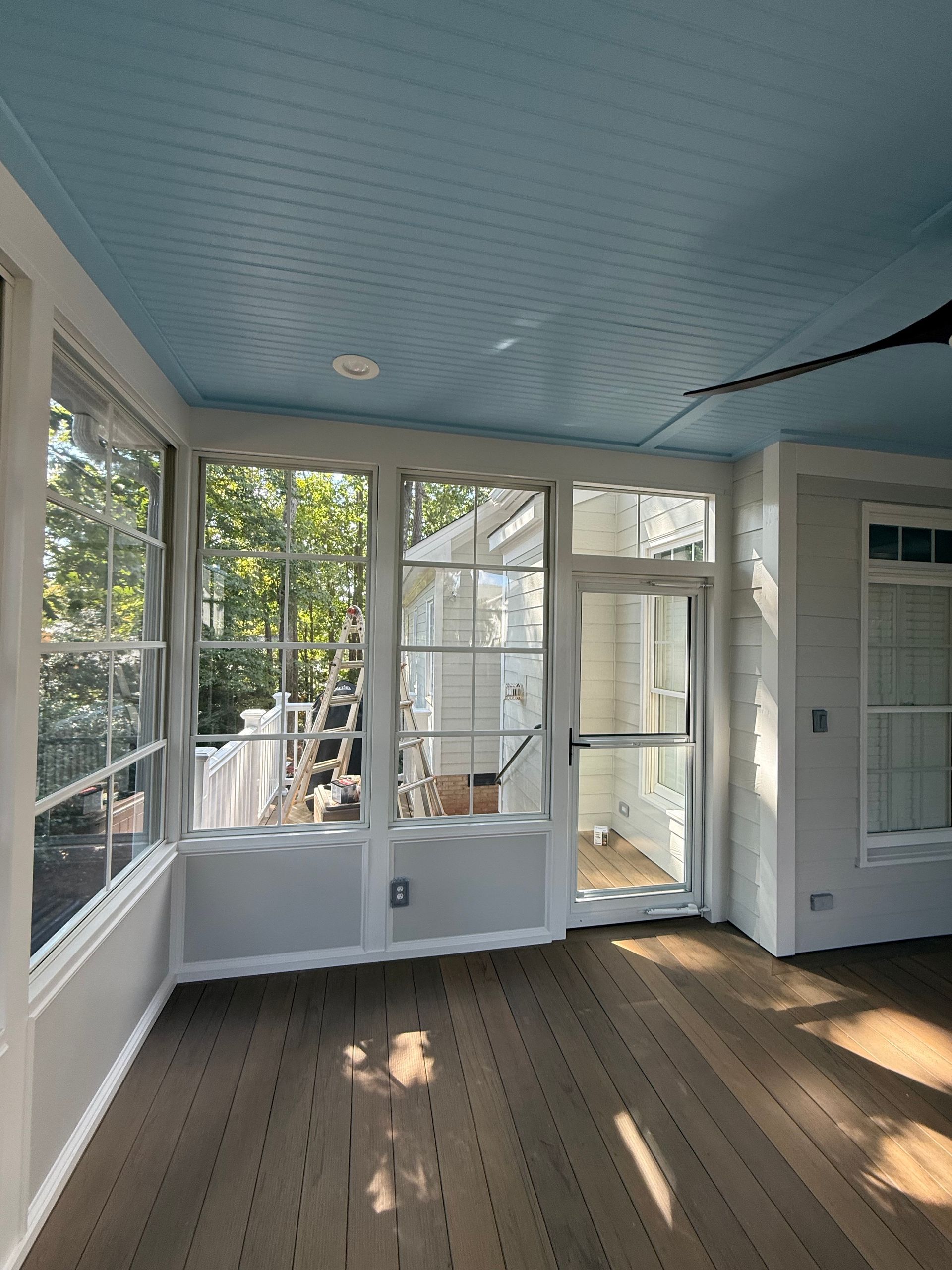 Sunroom interior with blue ceiling, white trim, and a brown wooden floor.