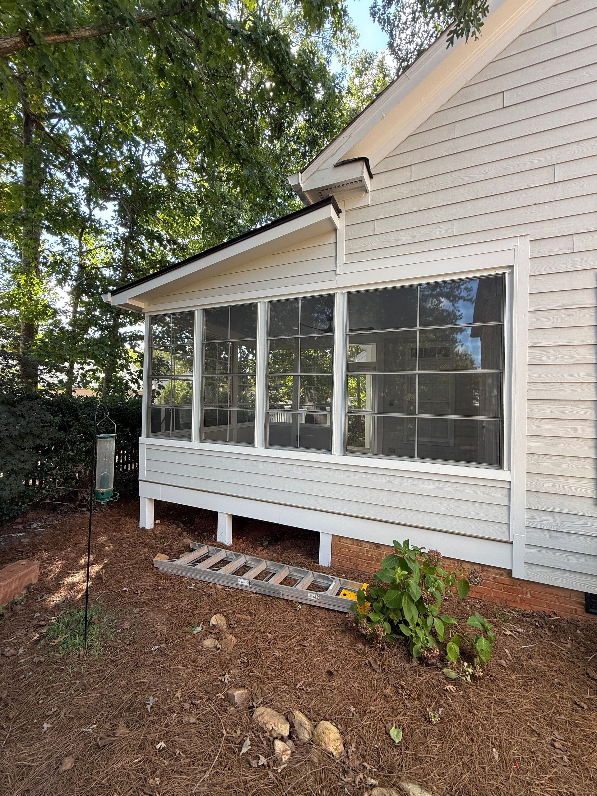 Screened-in porch on a white house, with a black roof, brown mulch, and a ladder at the base.