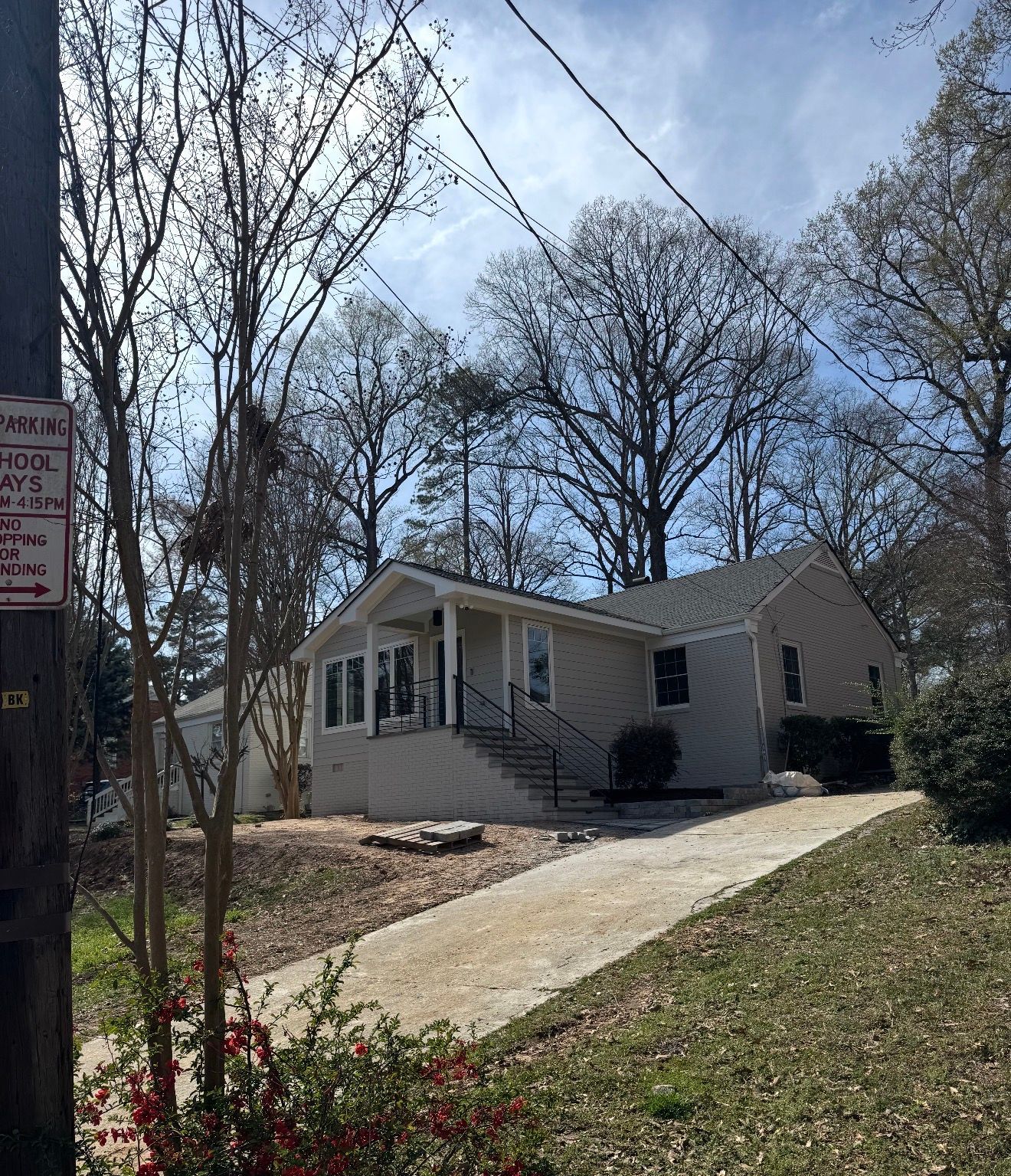 Tan house with a concrete driveway, surrounded by trees and a utility pole. Clear blue sky.