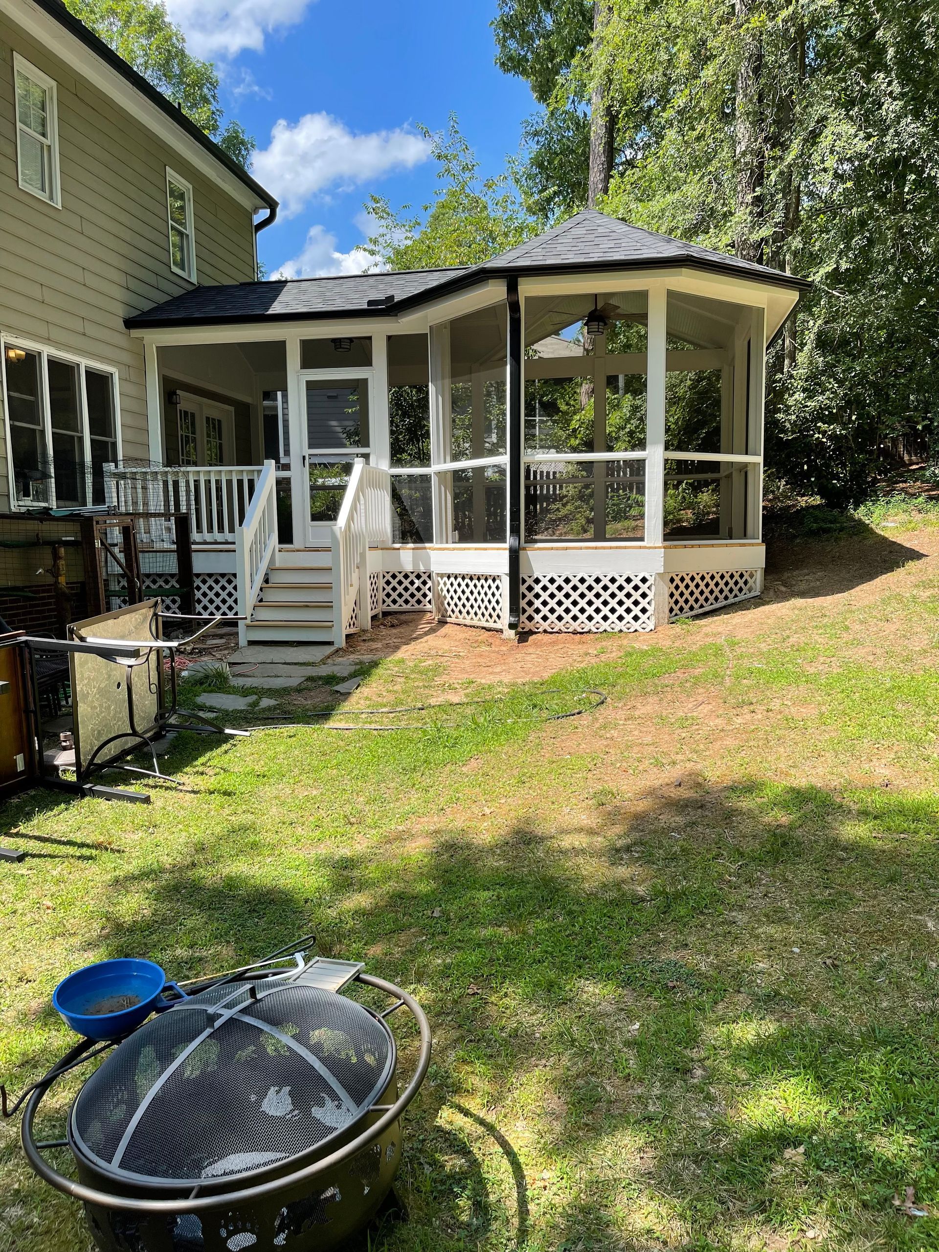 A screened-in porch with white railings and a gazebo-like roof attached to a light green house.