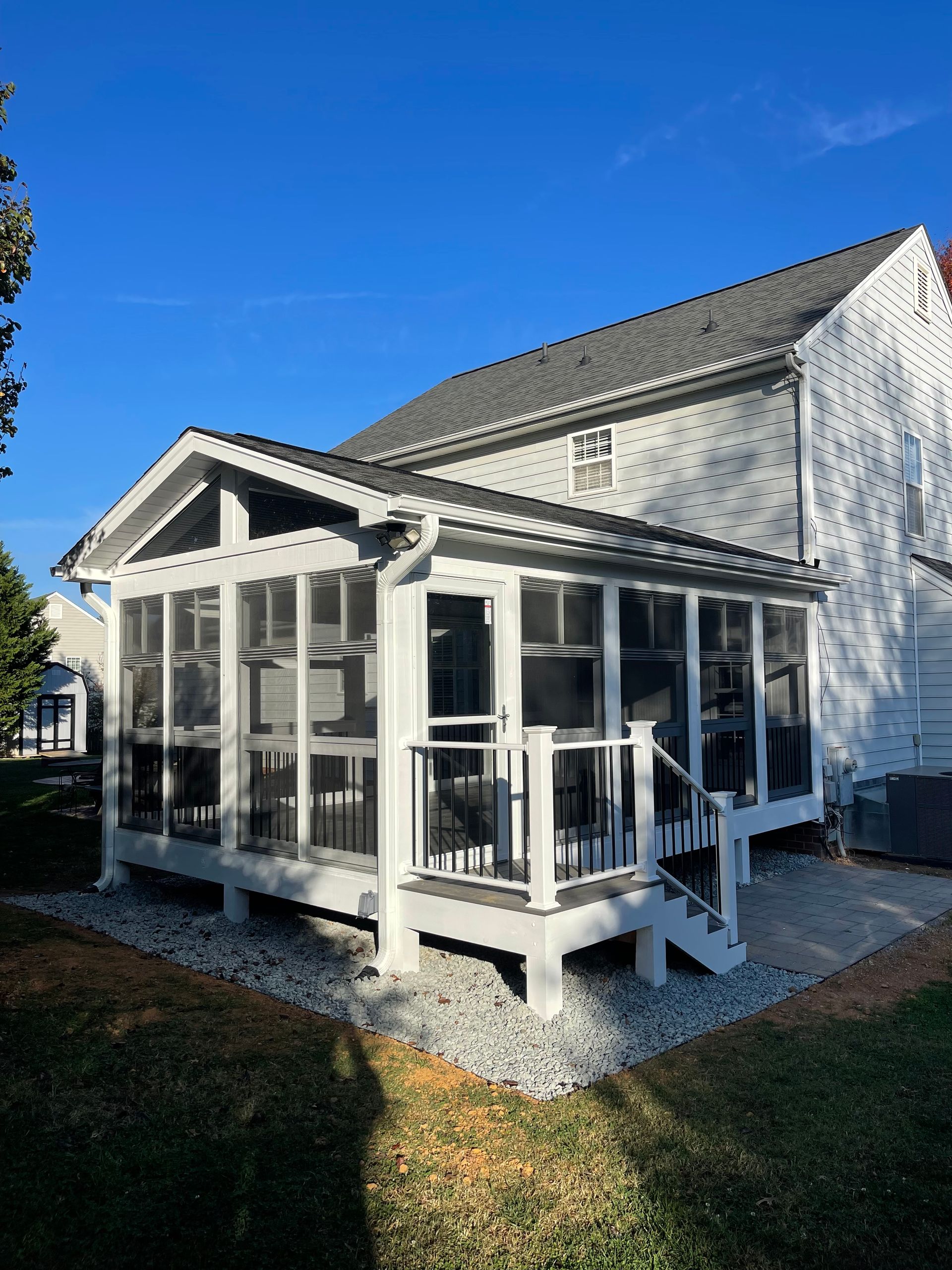 White screened-in porch attached to a two-story house, steps lead down, gray gravel.