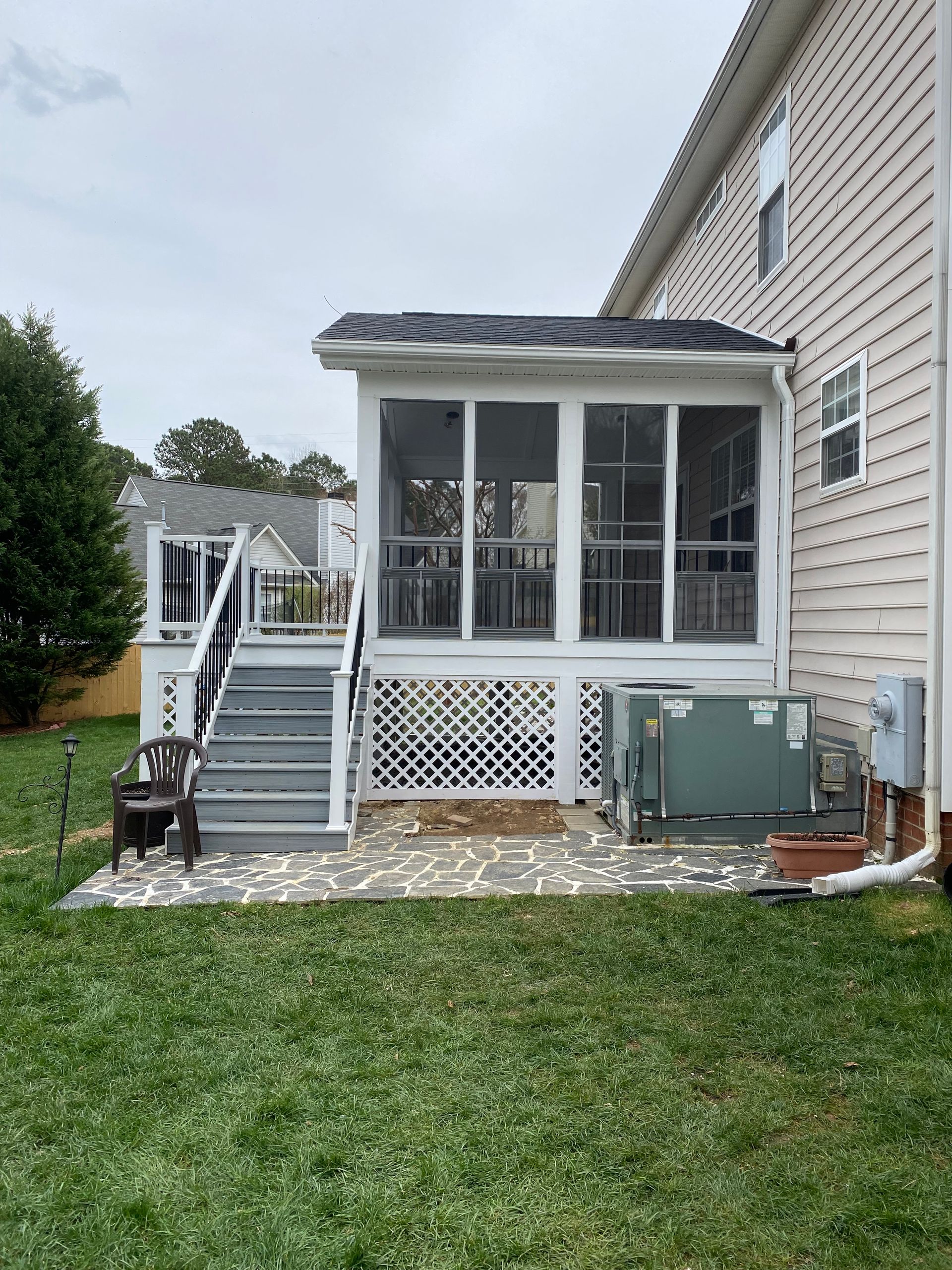 Screened porch attached to a two-story beige house with stone patio and gray steps.