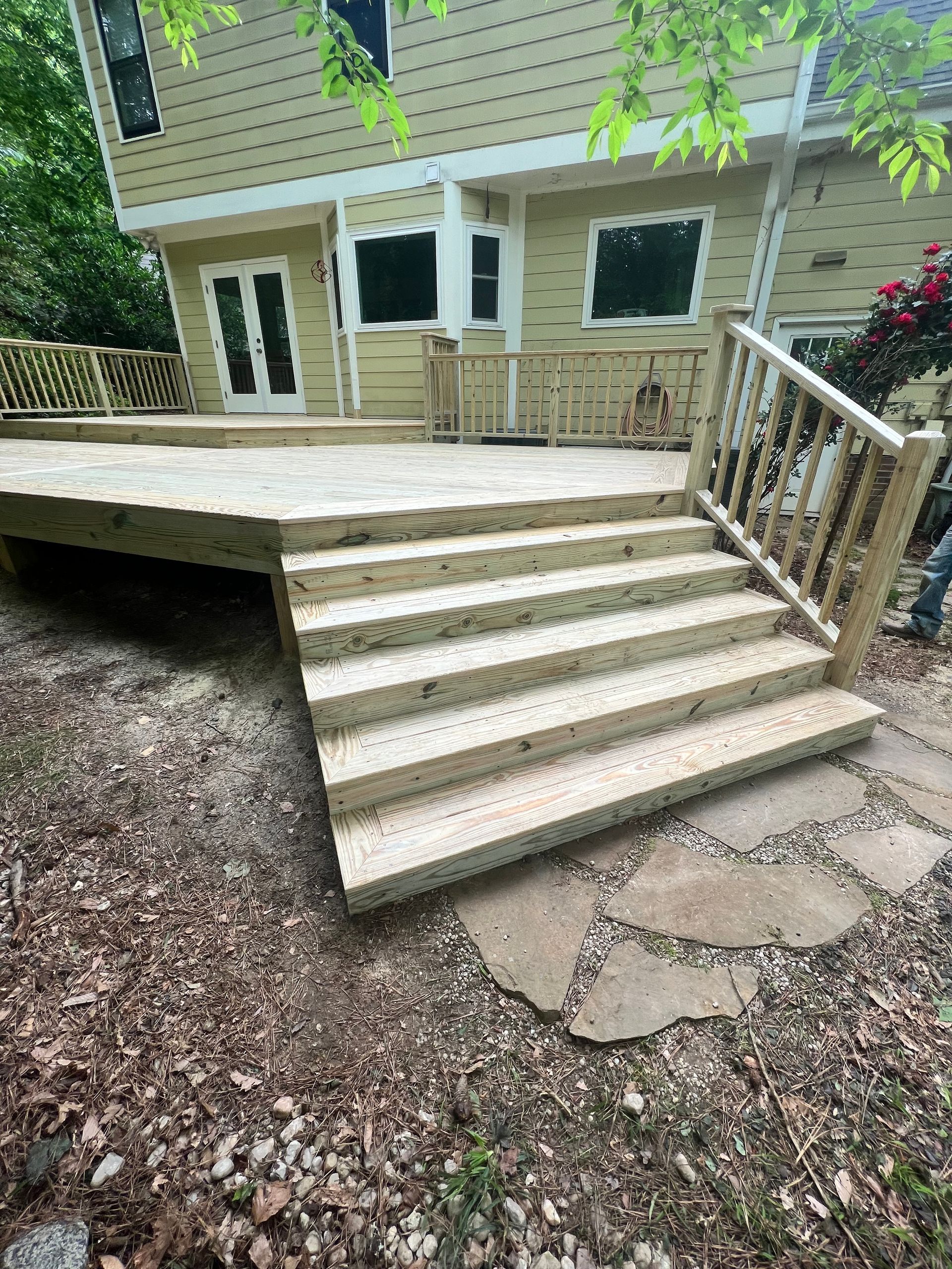 Wooden deck with steps leading down to stone pathway, house in background.