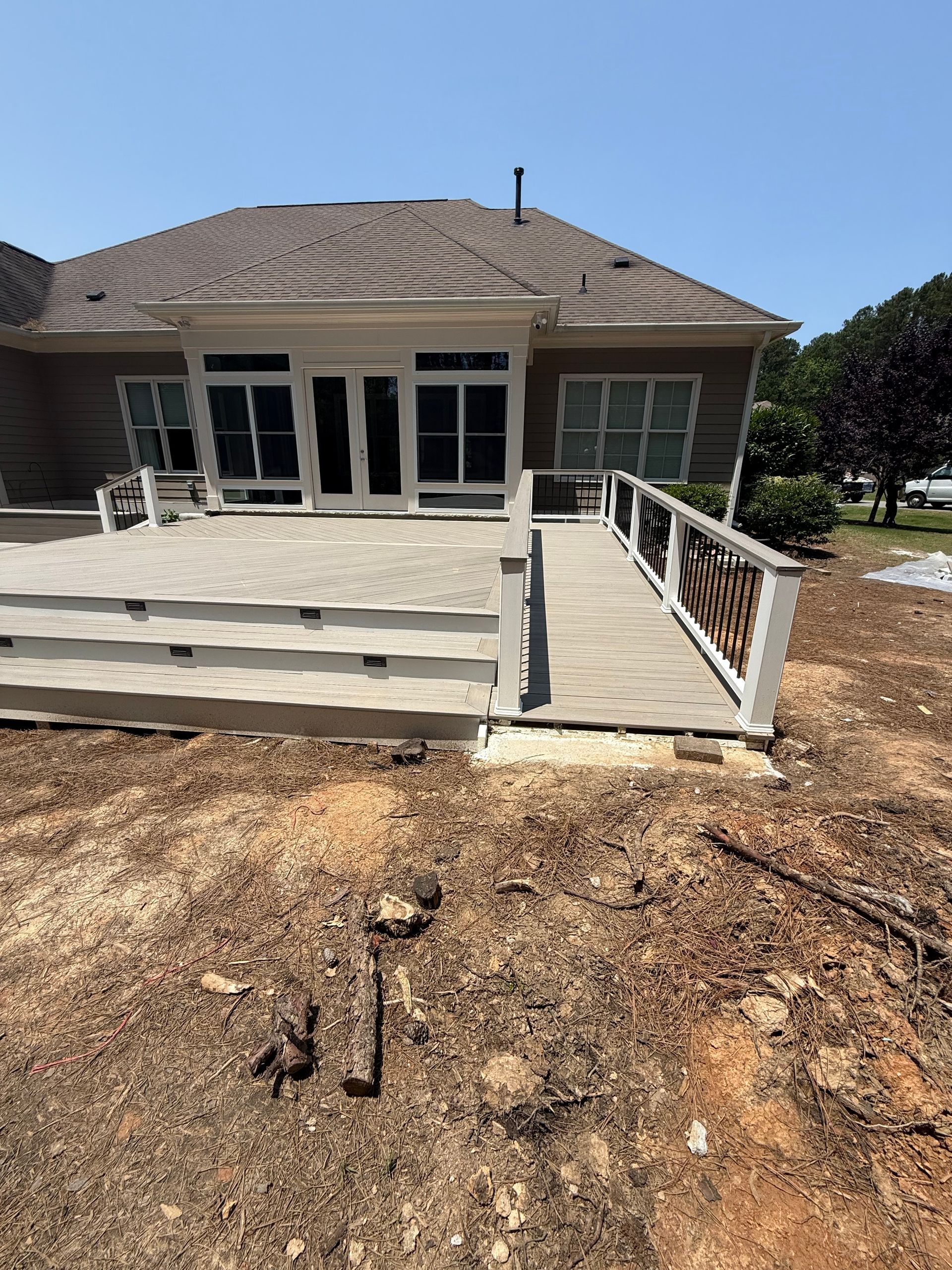 Deck with ramp and steps in front of a light brown house on a sunny day.