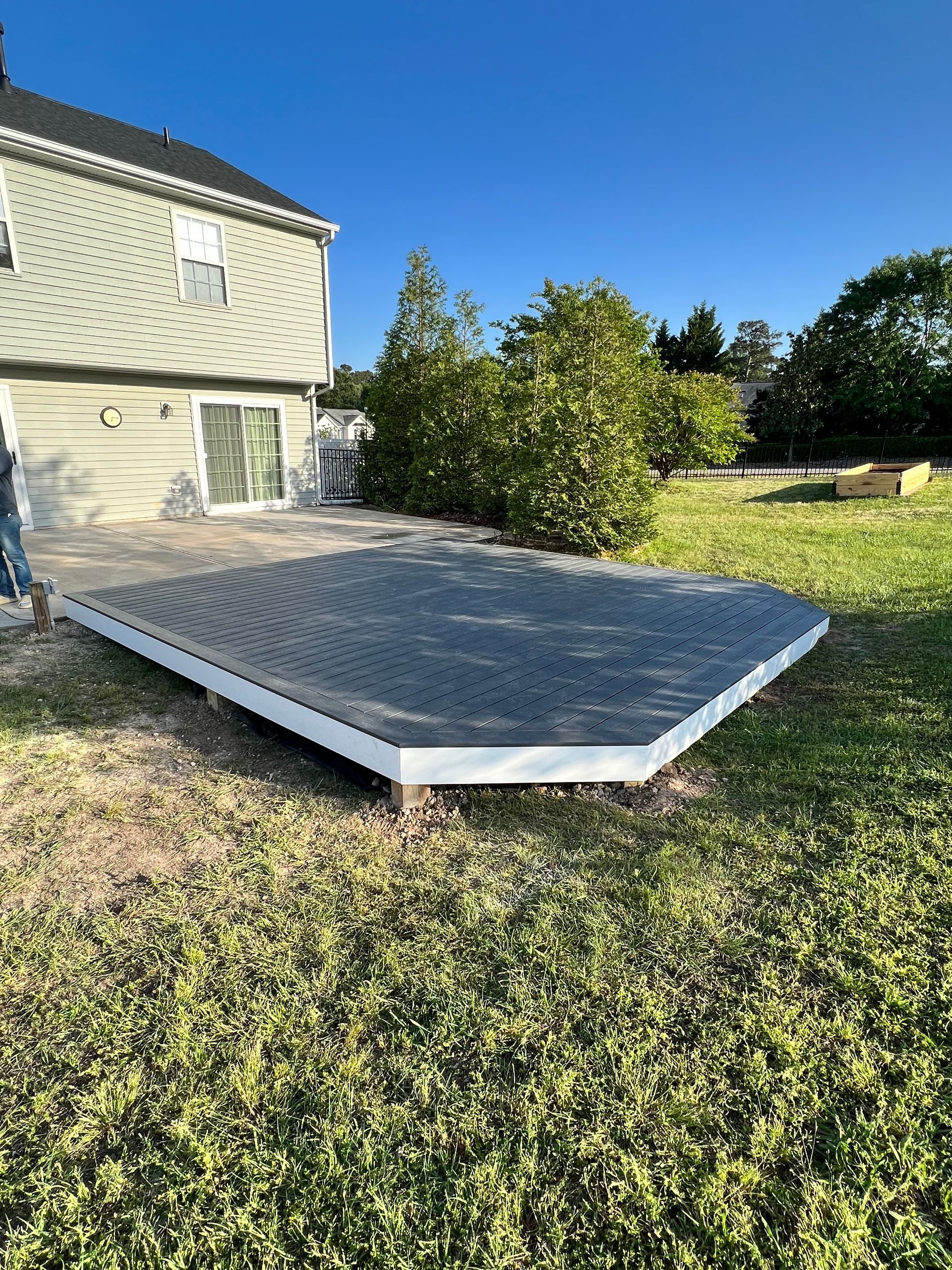 A newly built gray deck in a backyard, with a white frame and beige house in the background.