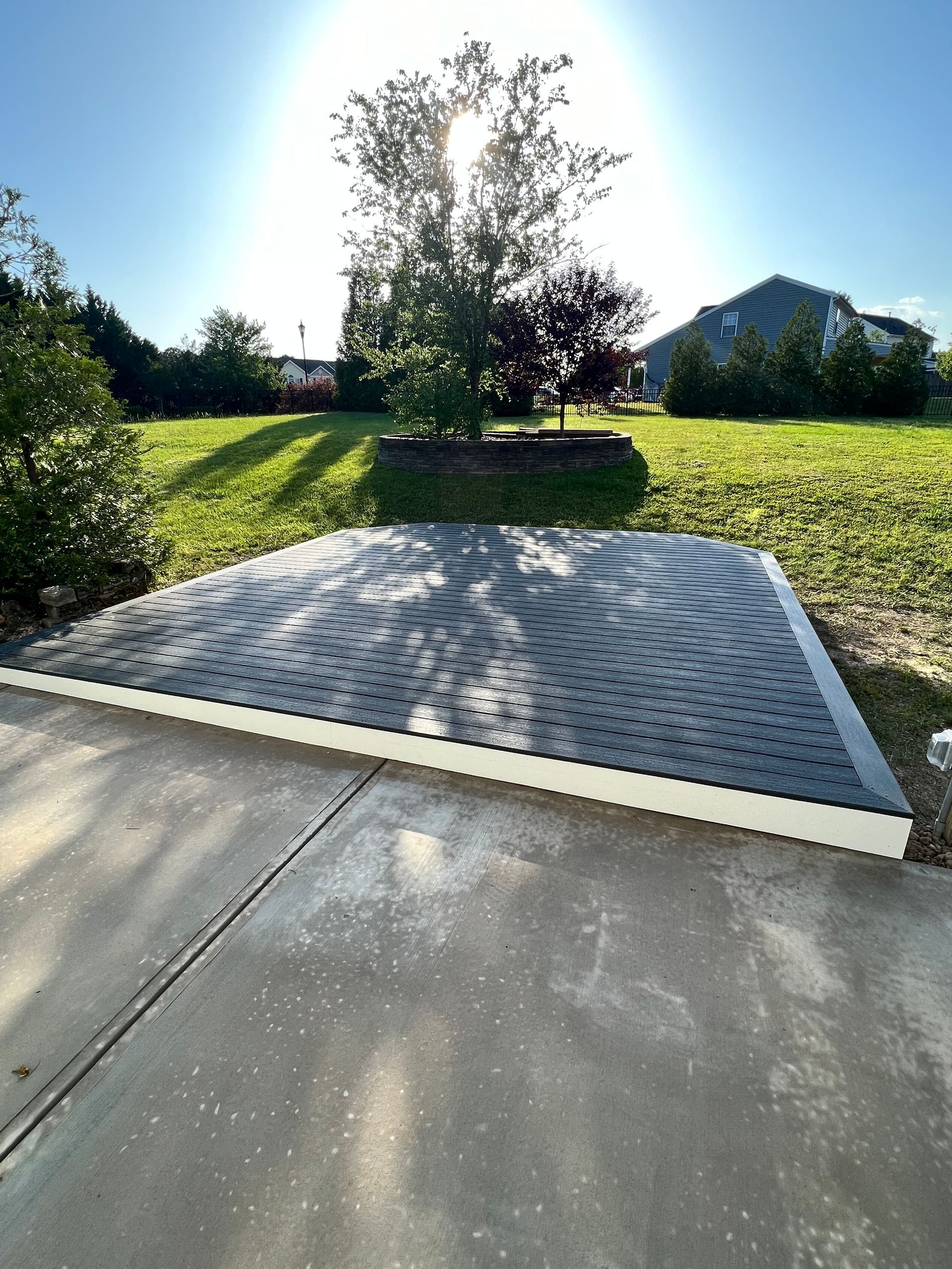 Backyard patio with a grey roof covering, grassy lawn, and a tree under a bright sun.