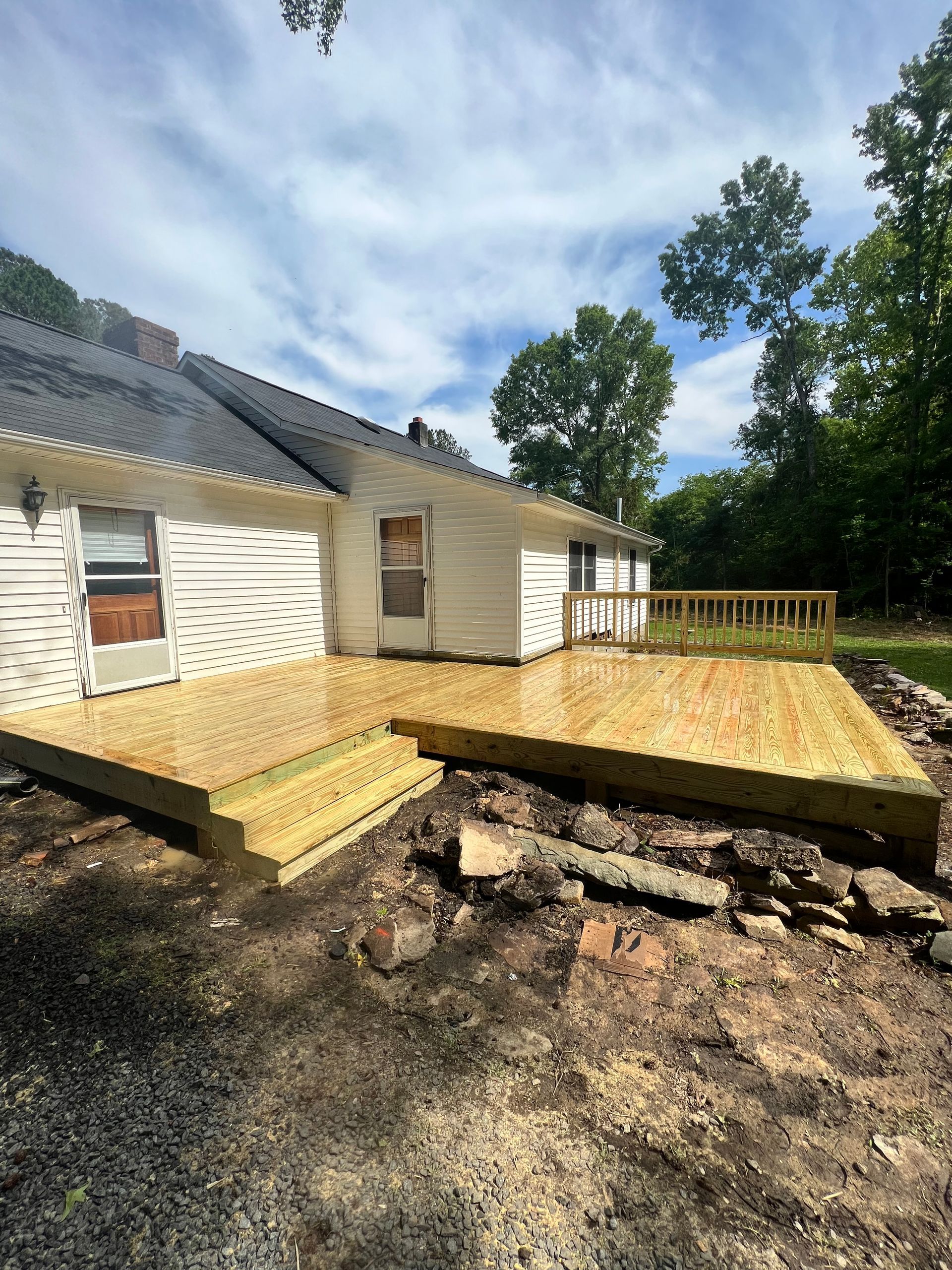 Newly built wooden deck attached to a white house, with steps leading down to a yard.