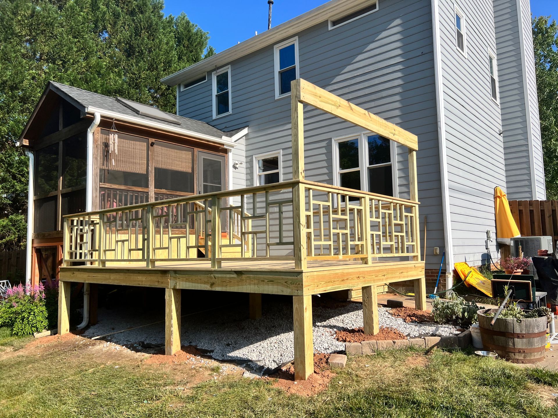 Newly built wooden deck with intricate railing attached to a two-story gray house.