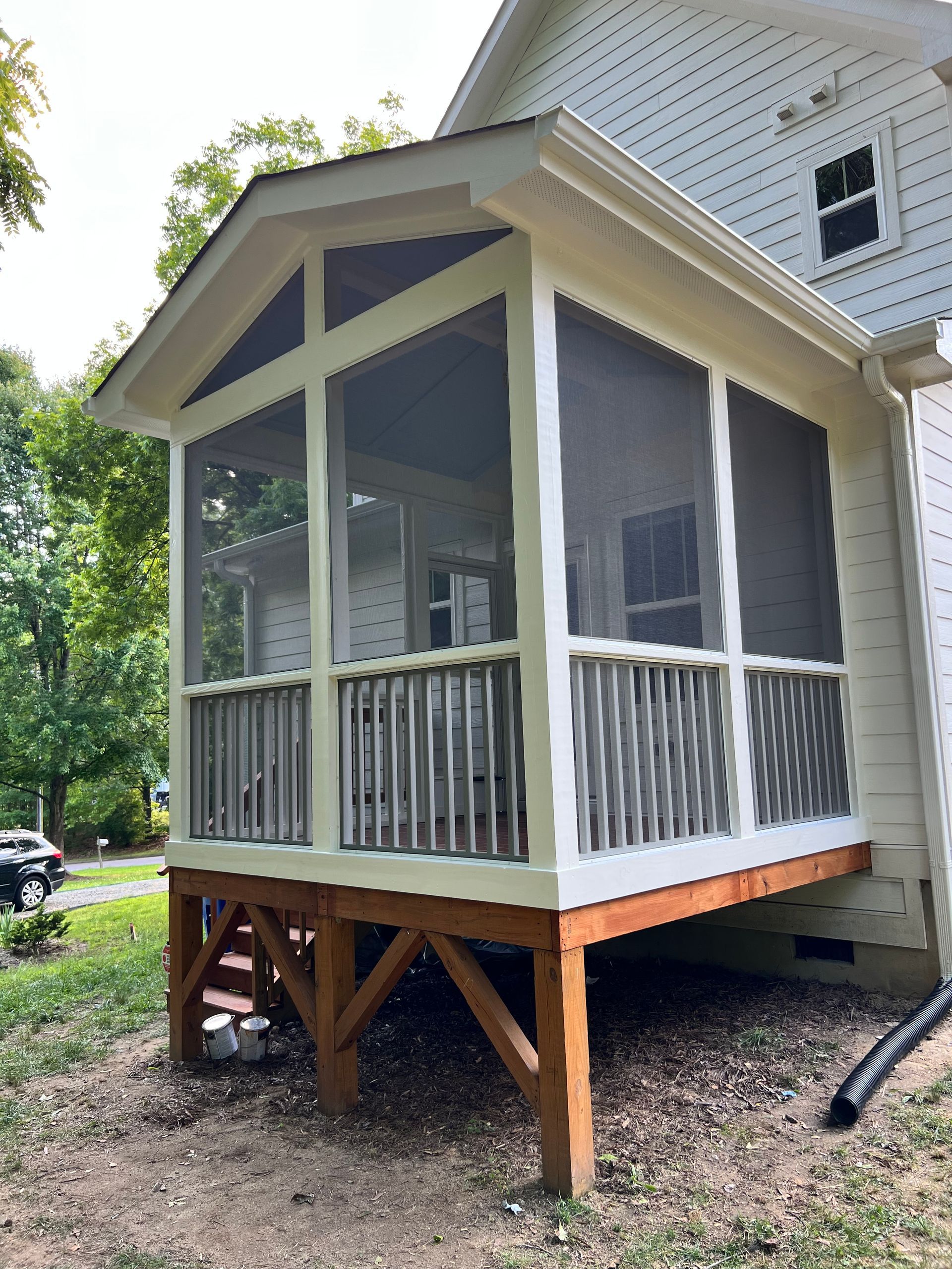 Screened porch addition with a wooden deck, connected to a light-colored house.