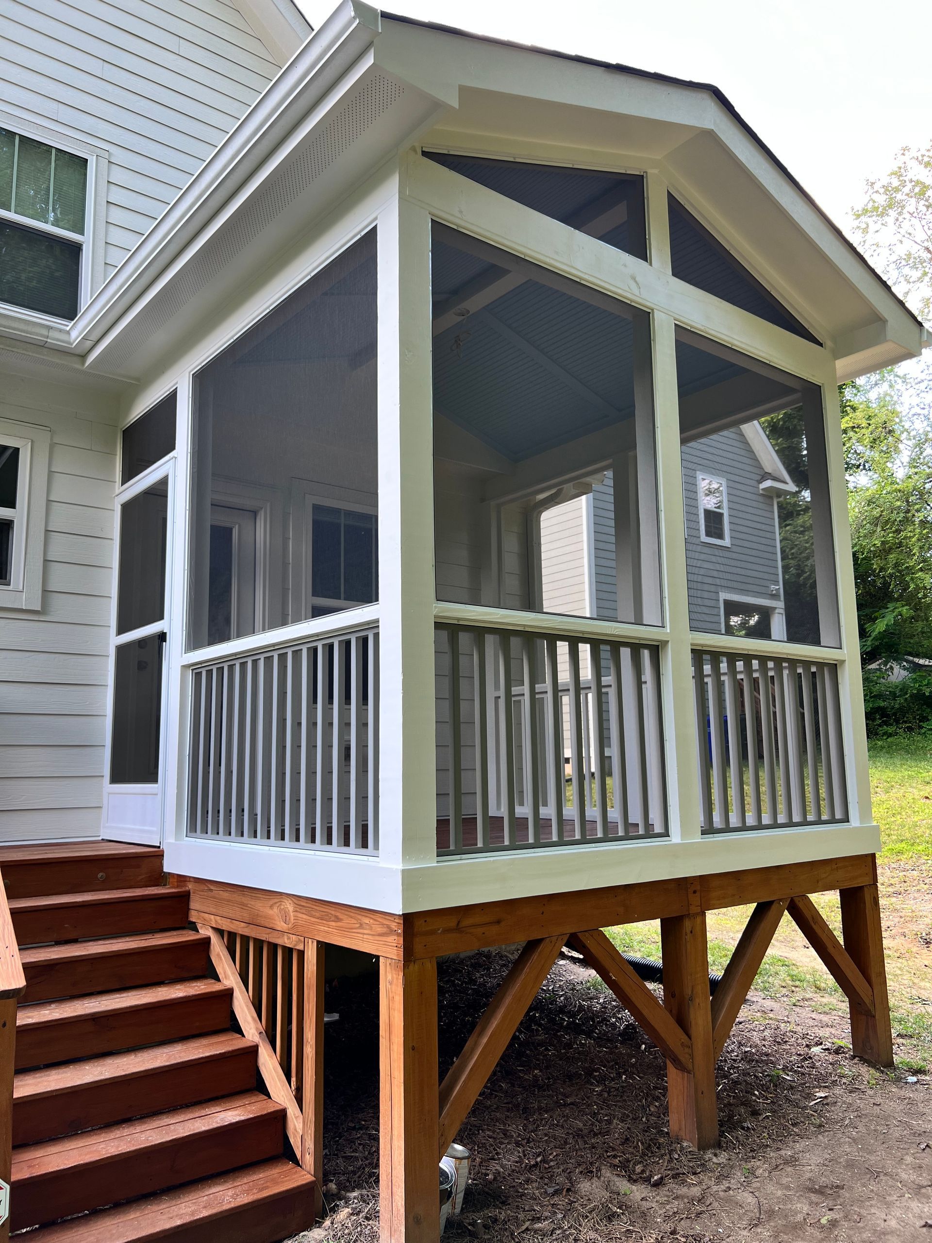Screened porch with wooden stairs, railings, and brown supports; tan siding on the house.