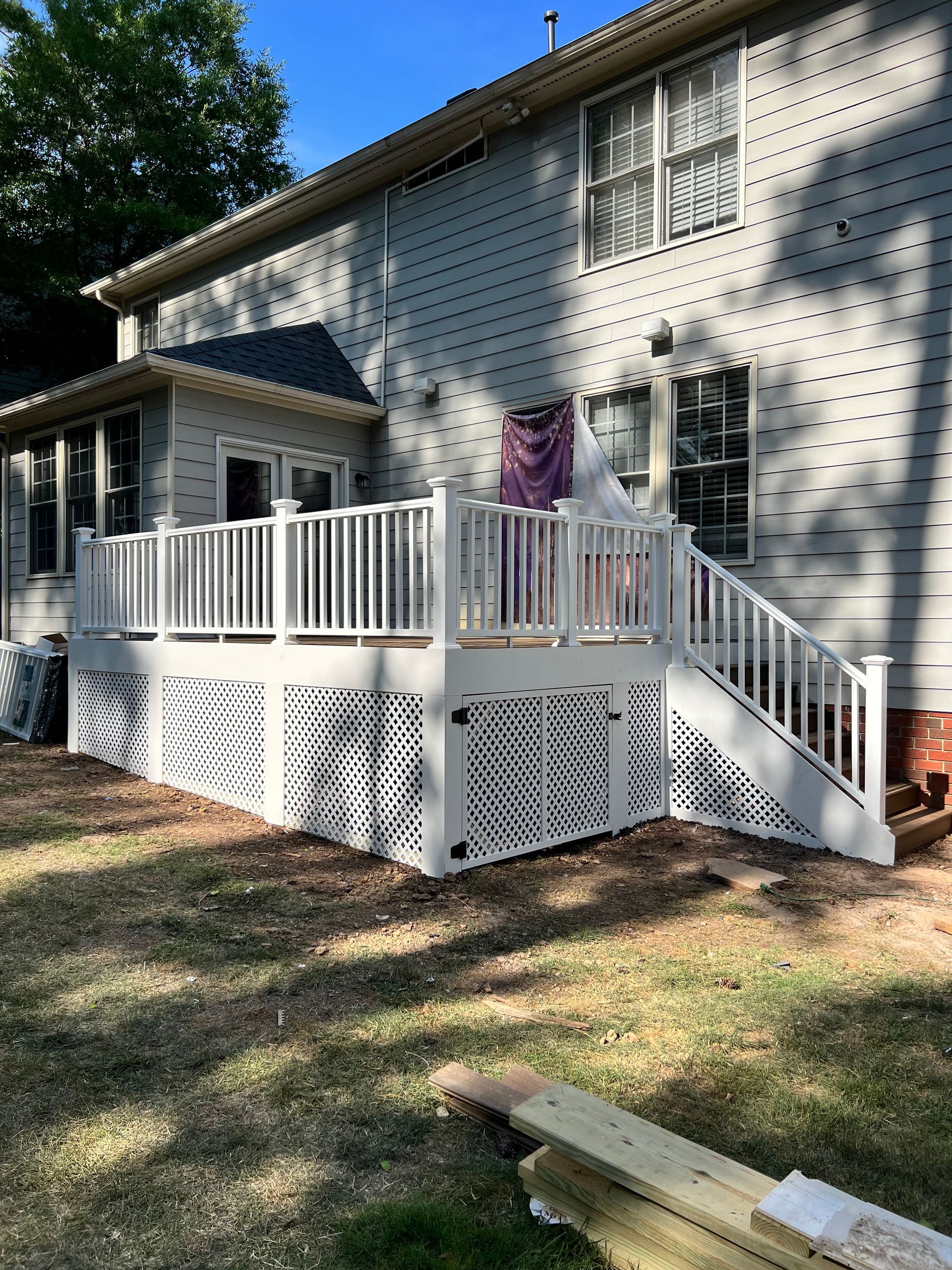 White deck with lattice skirt and railing, stairs, attached to a light gray house.