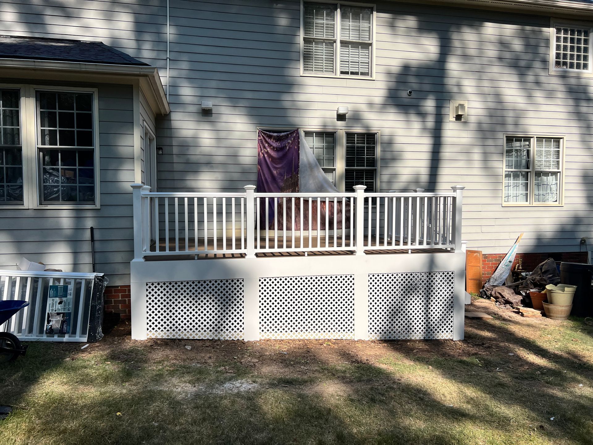White deck with lattice skirting against a light blue house with several windows.