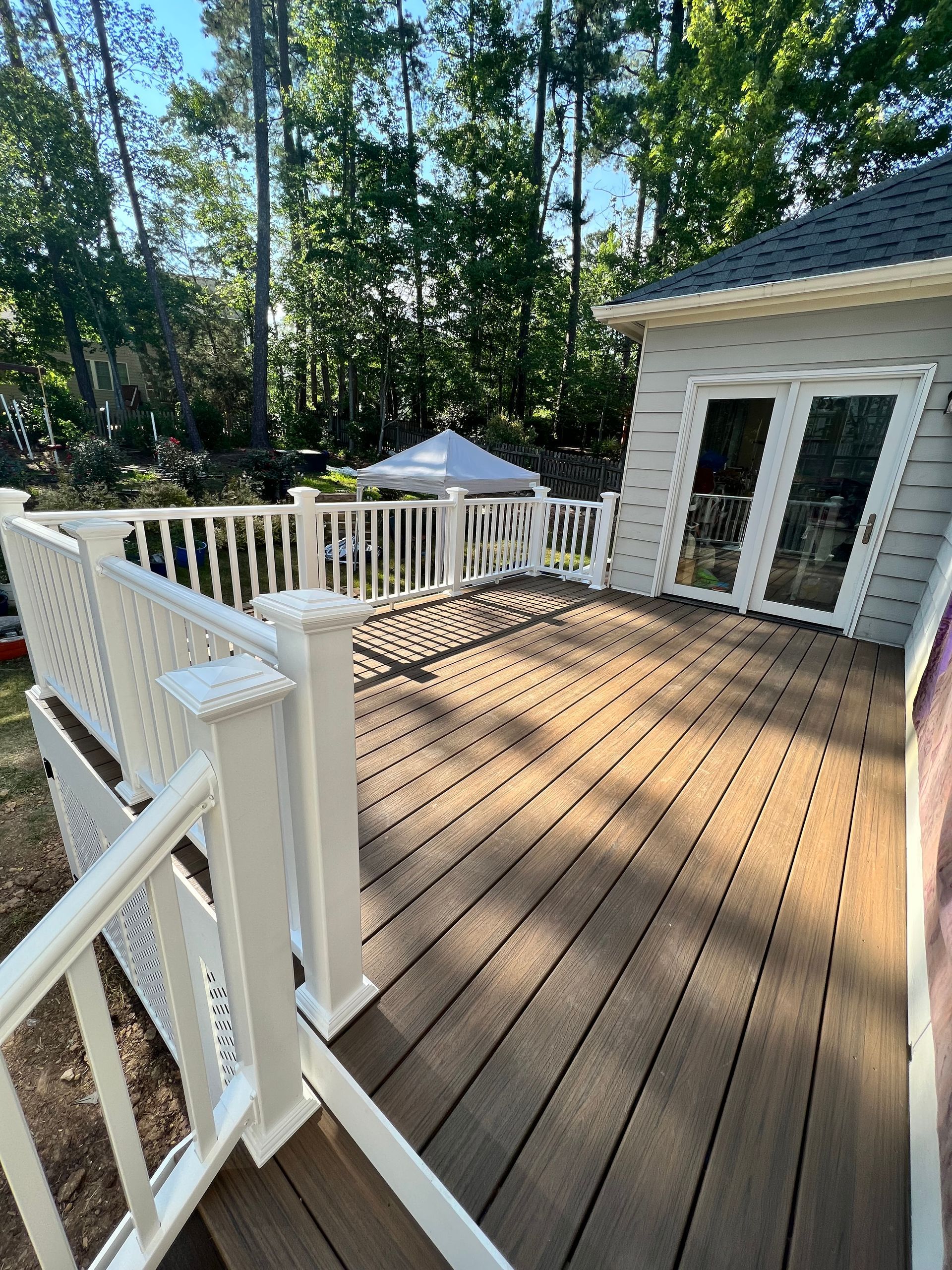 Wooden deck with white railing, leading to a building with glass doors and a tent in the background.