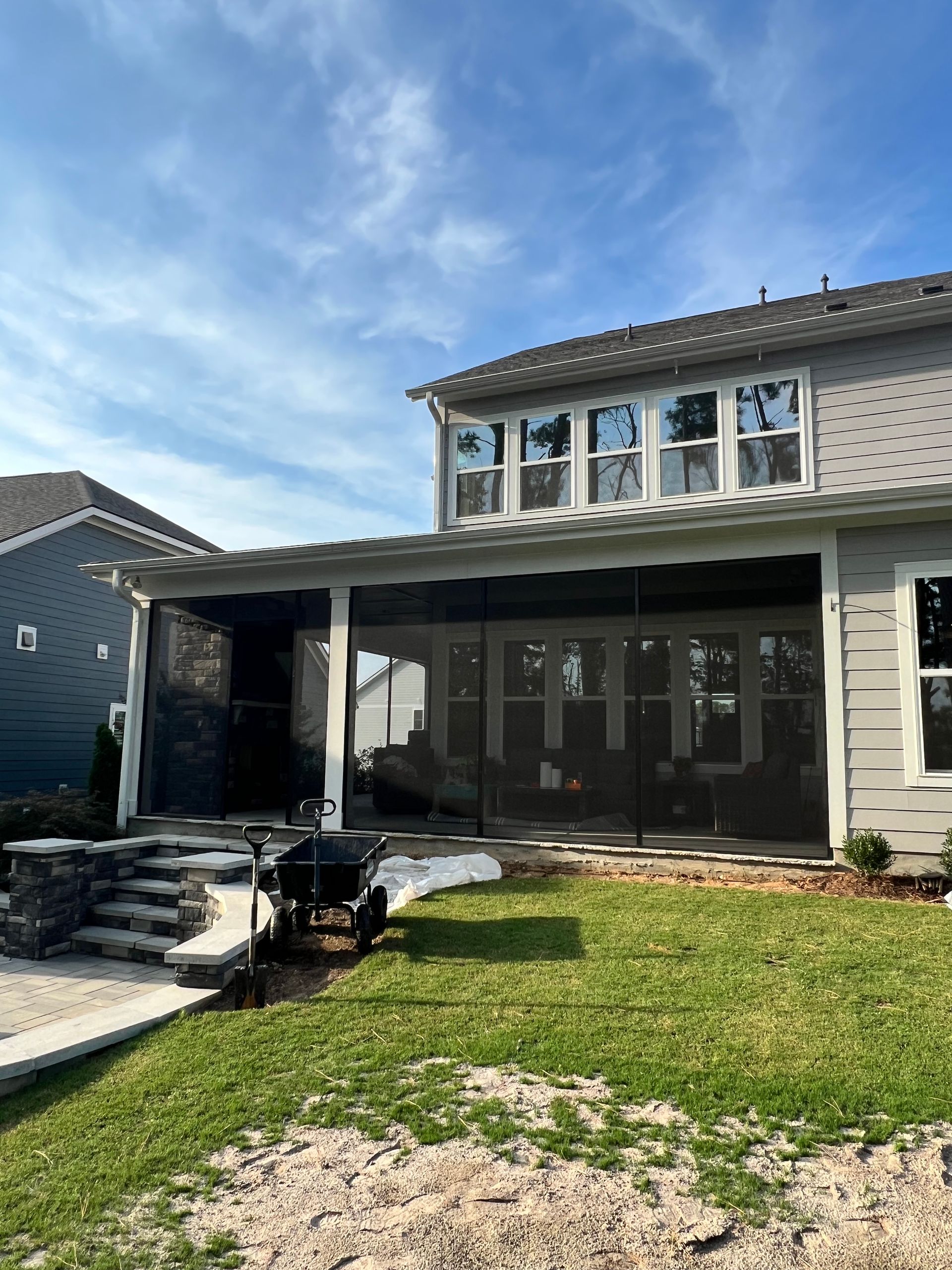 A house with a screened porch, gray siding, green lawn, and a bright blue sky.