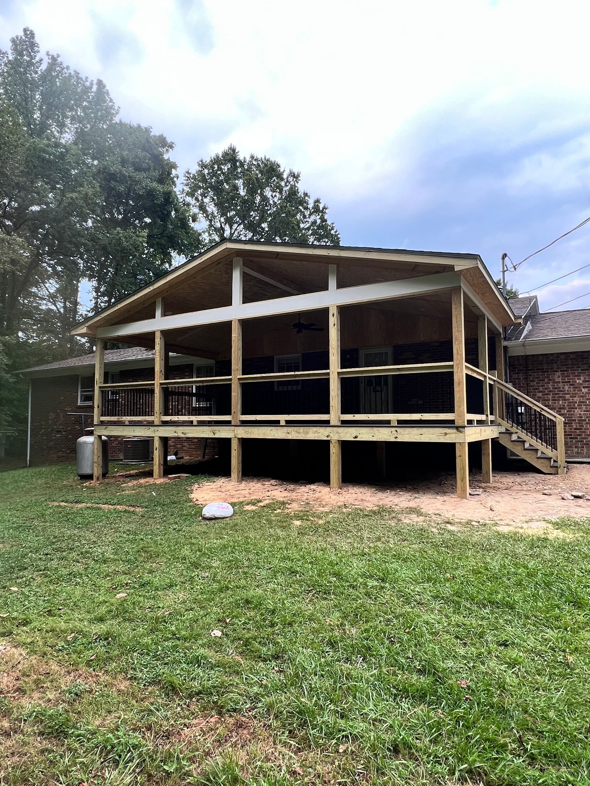 Wooden screened porch addition on a brick house; green grass in foreground, cloudy sky.