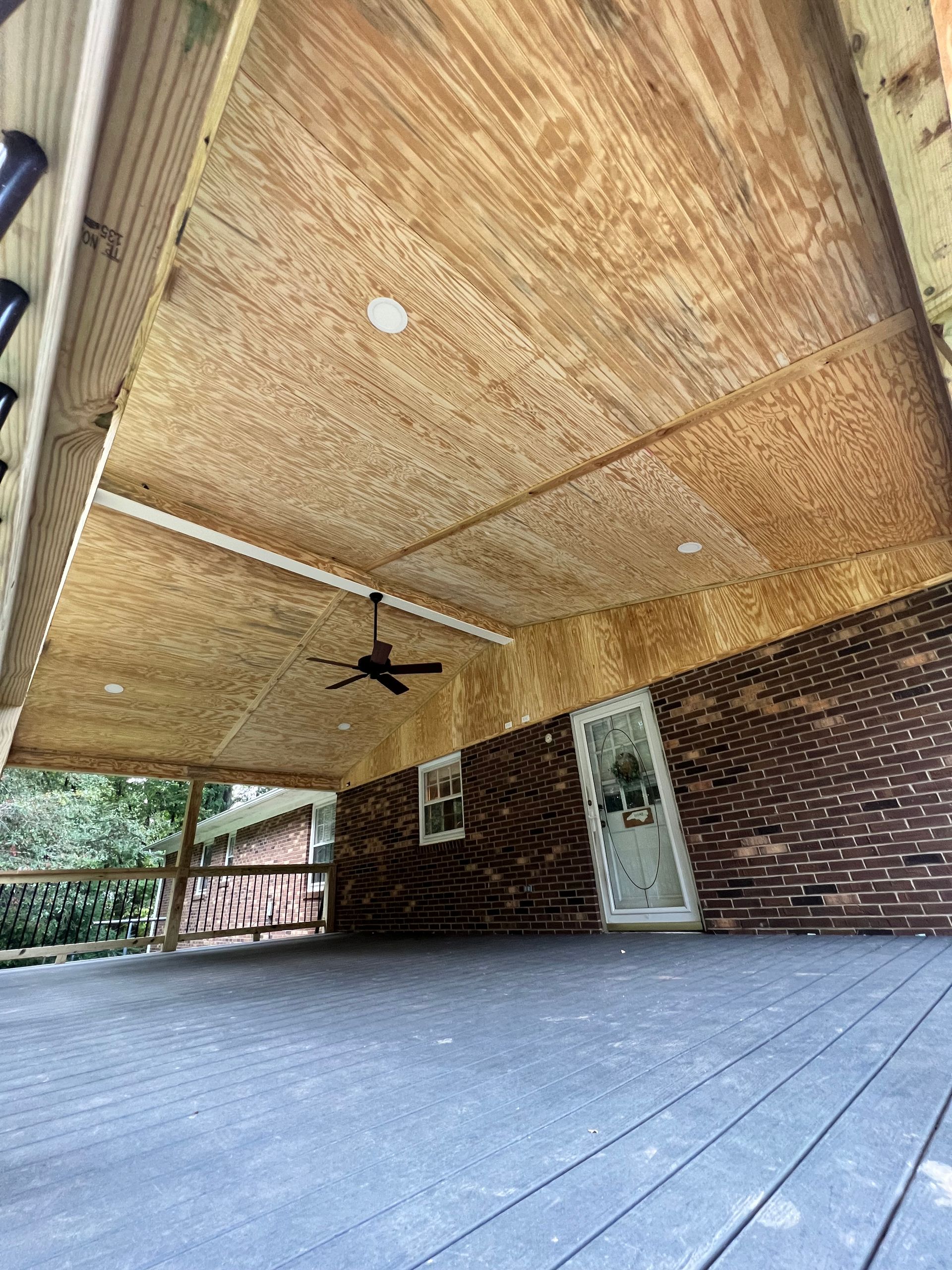 Covered deck with wood ceiling, brick wall, door, and fan; dark gray deck floor.