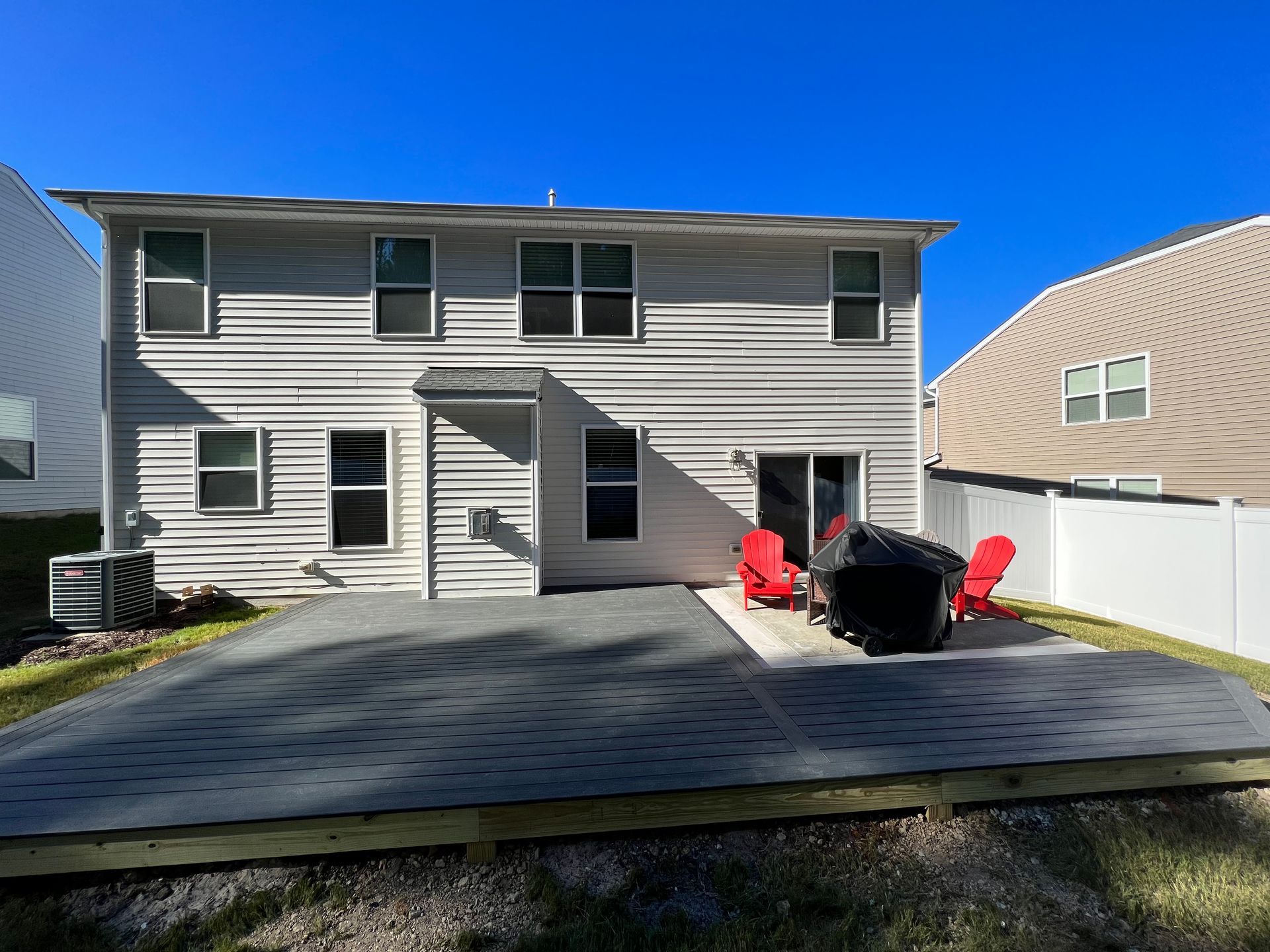 Back of a two-story house with gray siding, deck, and two red chairs.