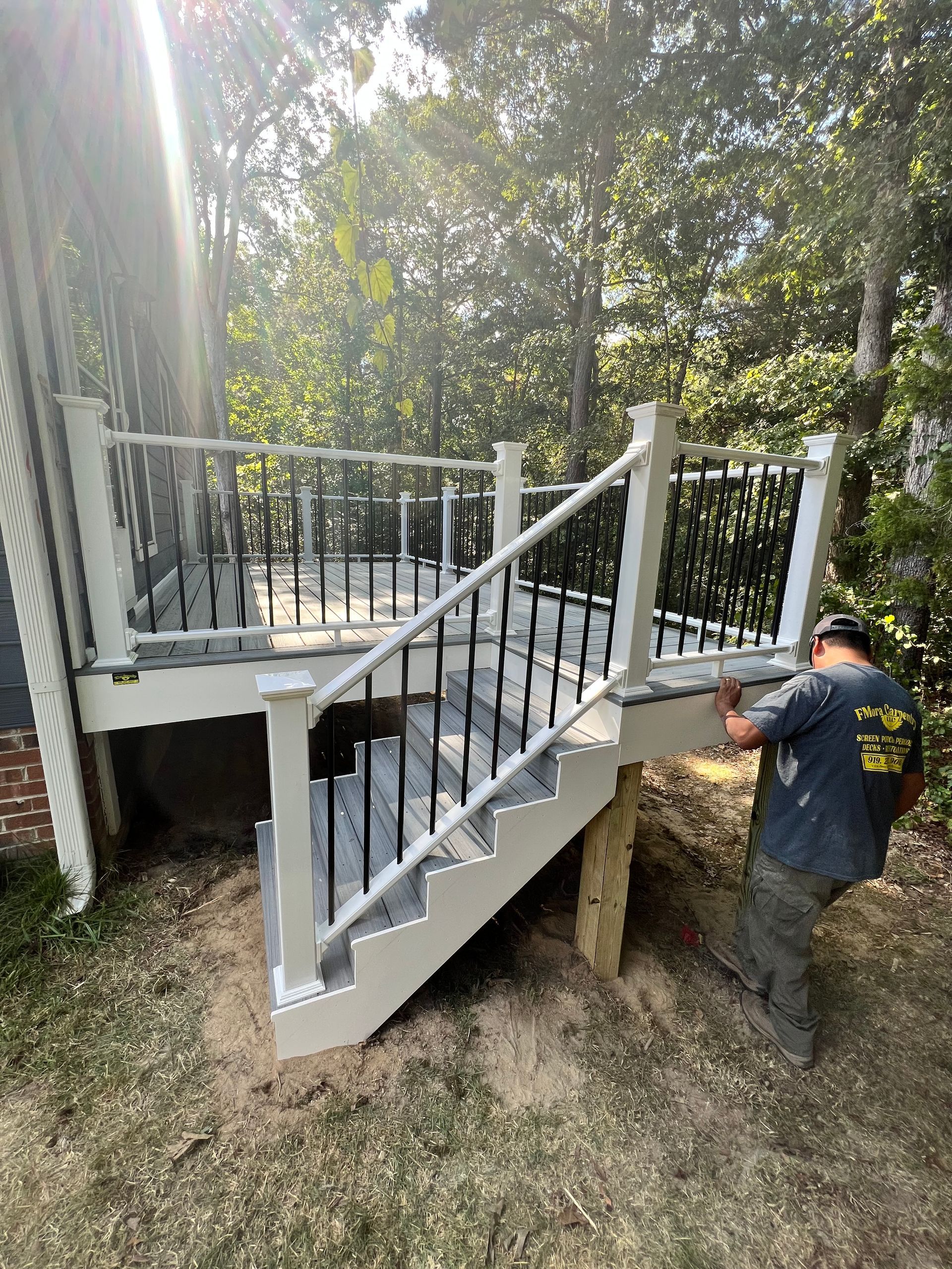 A man standing near a newly built deck with stairs. The deck has gray and white railings, black balusters.