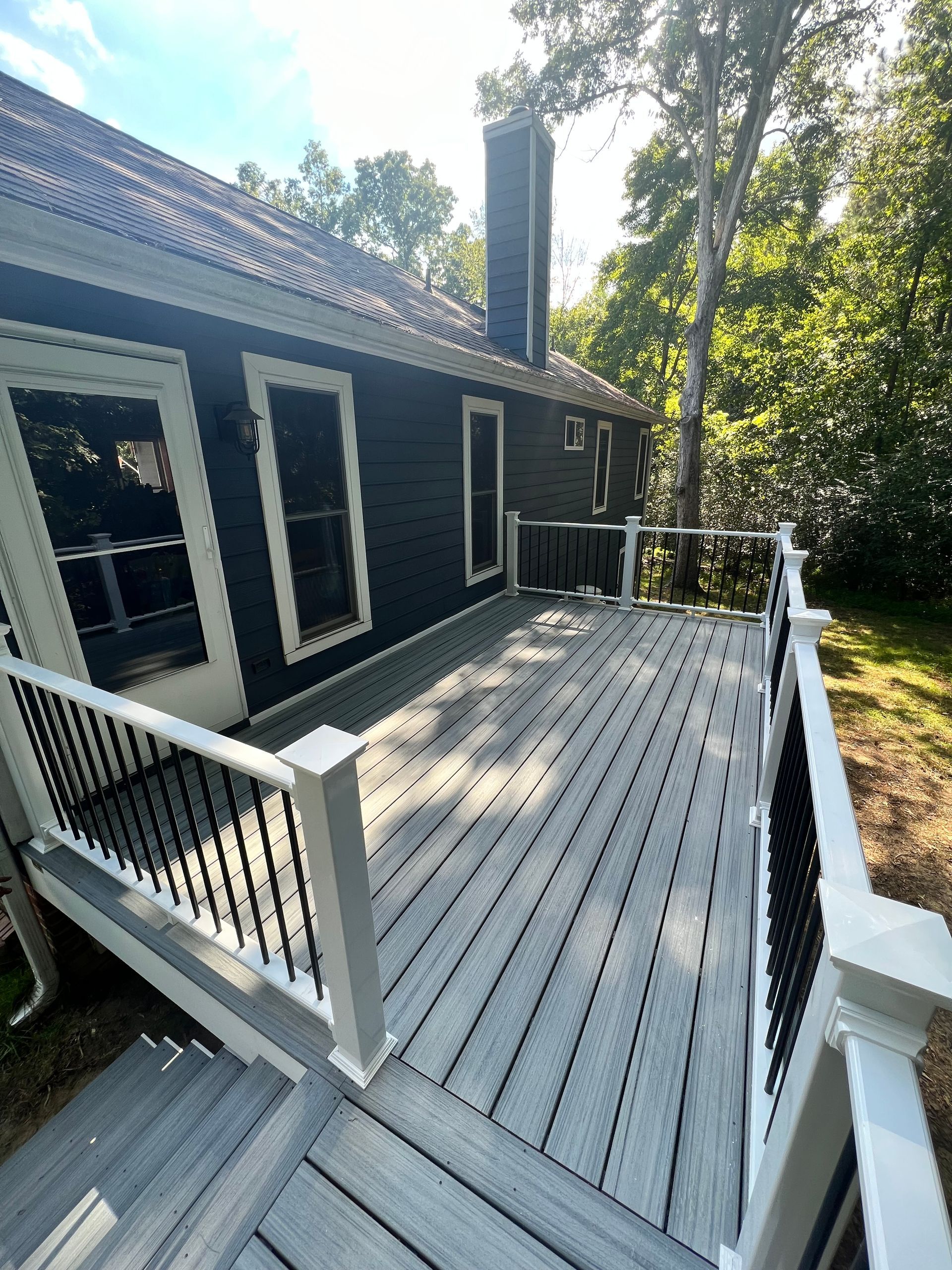 Gray composite deck with black railing attached to a dark-colored house with a chimney.