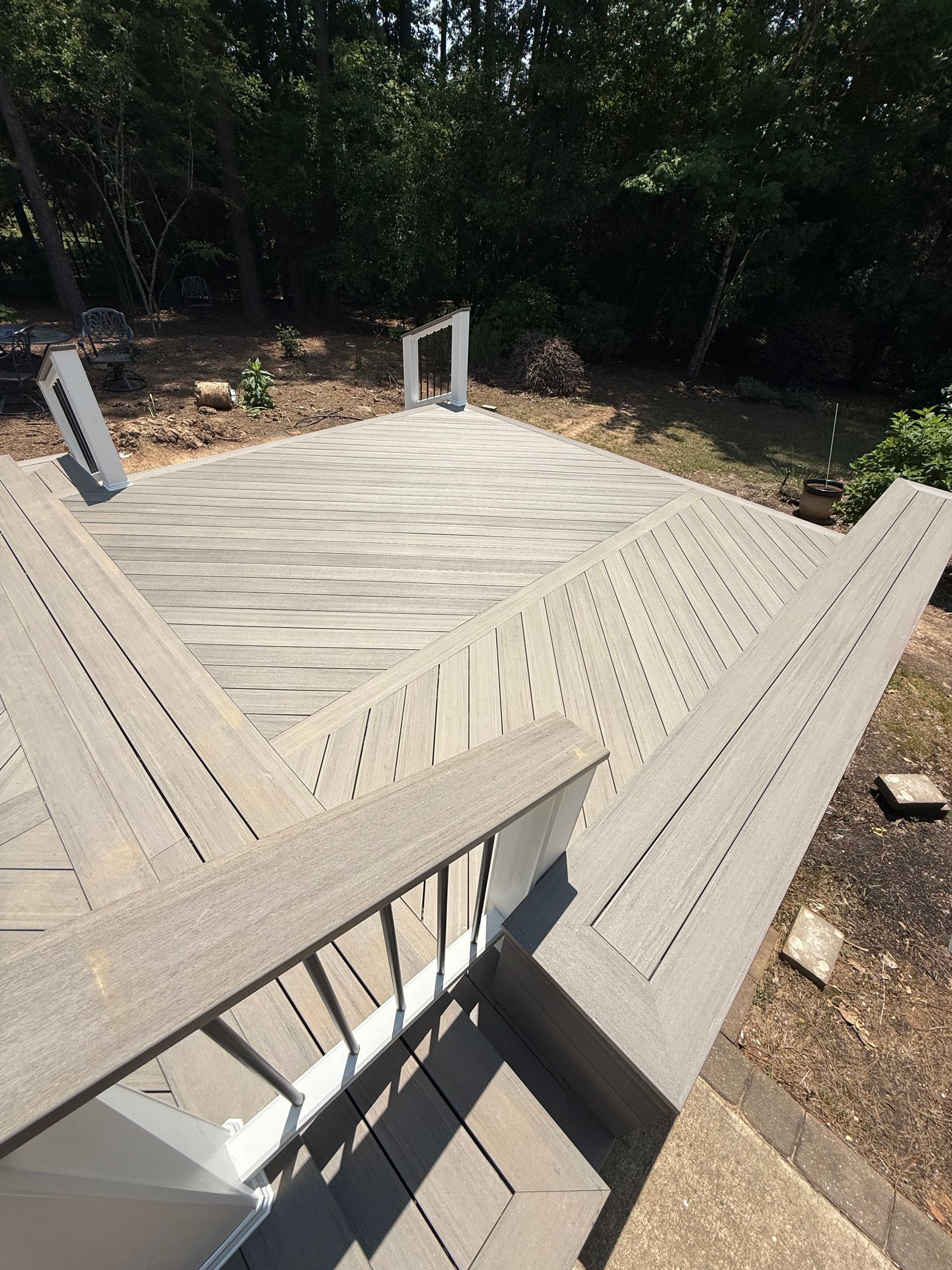 A newly constructed, angled deck with light gray composite boards and a white railing in a sunny backyard.