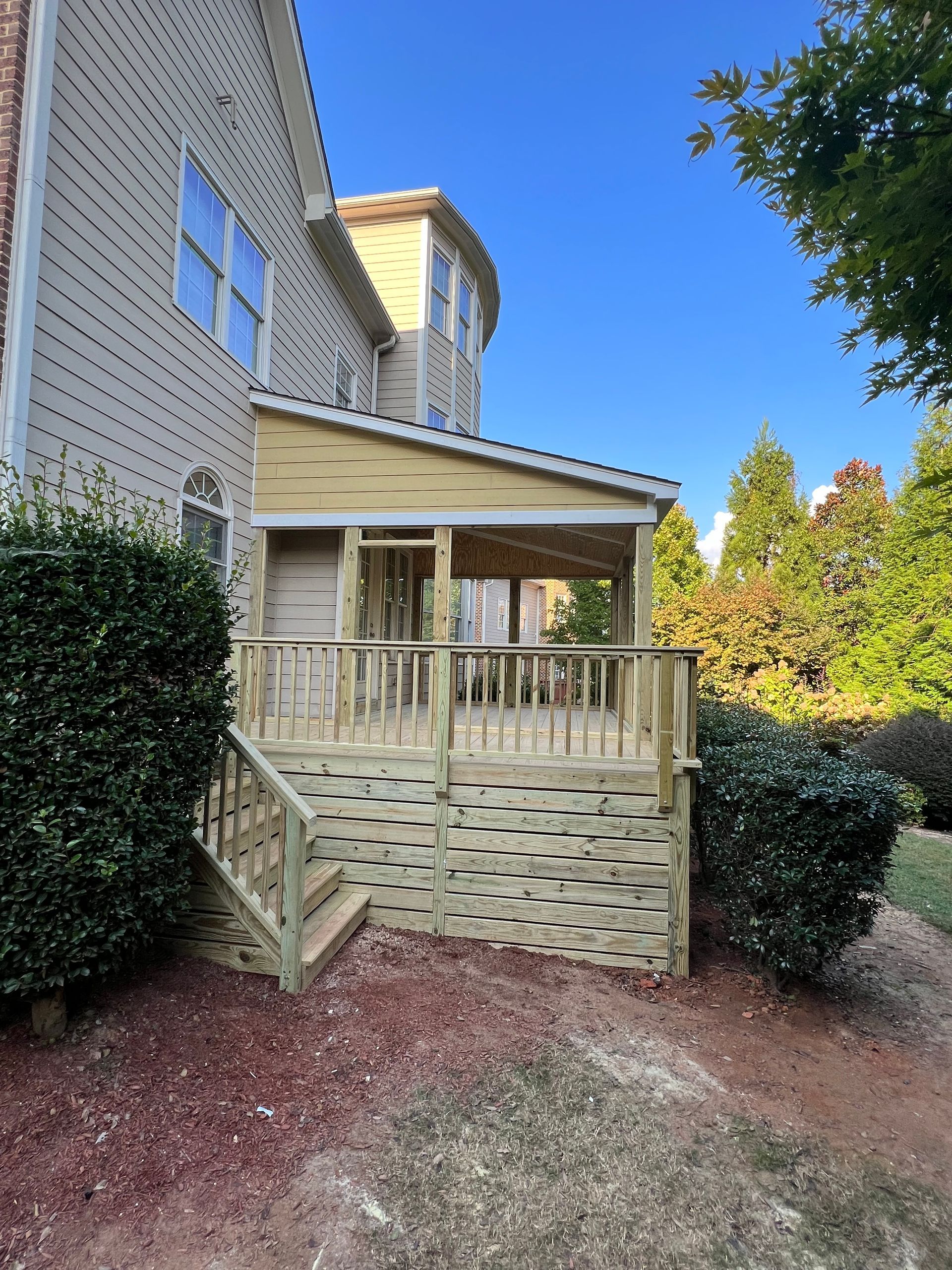 Wooden deck with stairs, attached to a house with an overhanging roof.