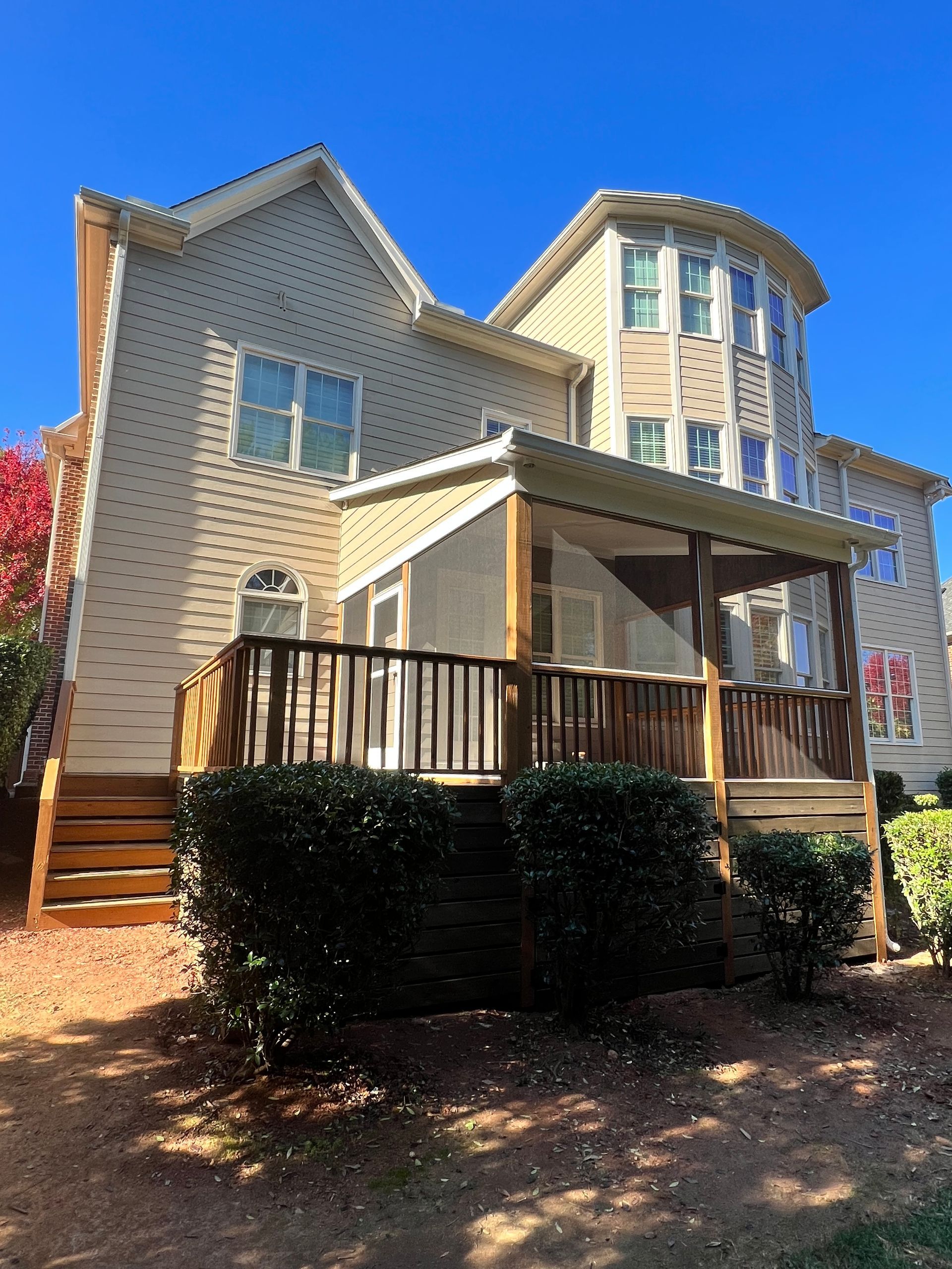 Back of a beige house with a wooden deck and screened porch on a sunny day.