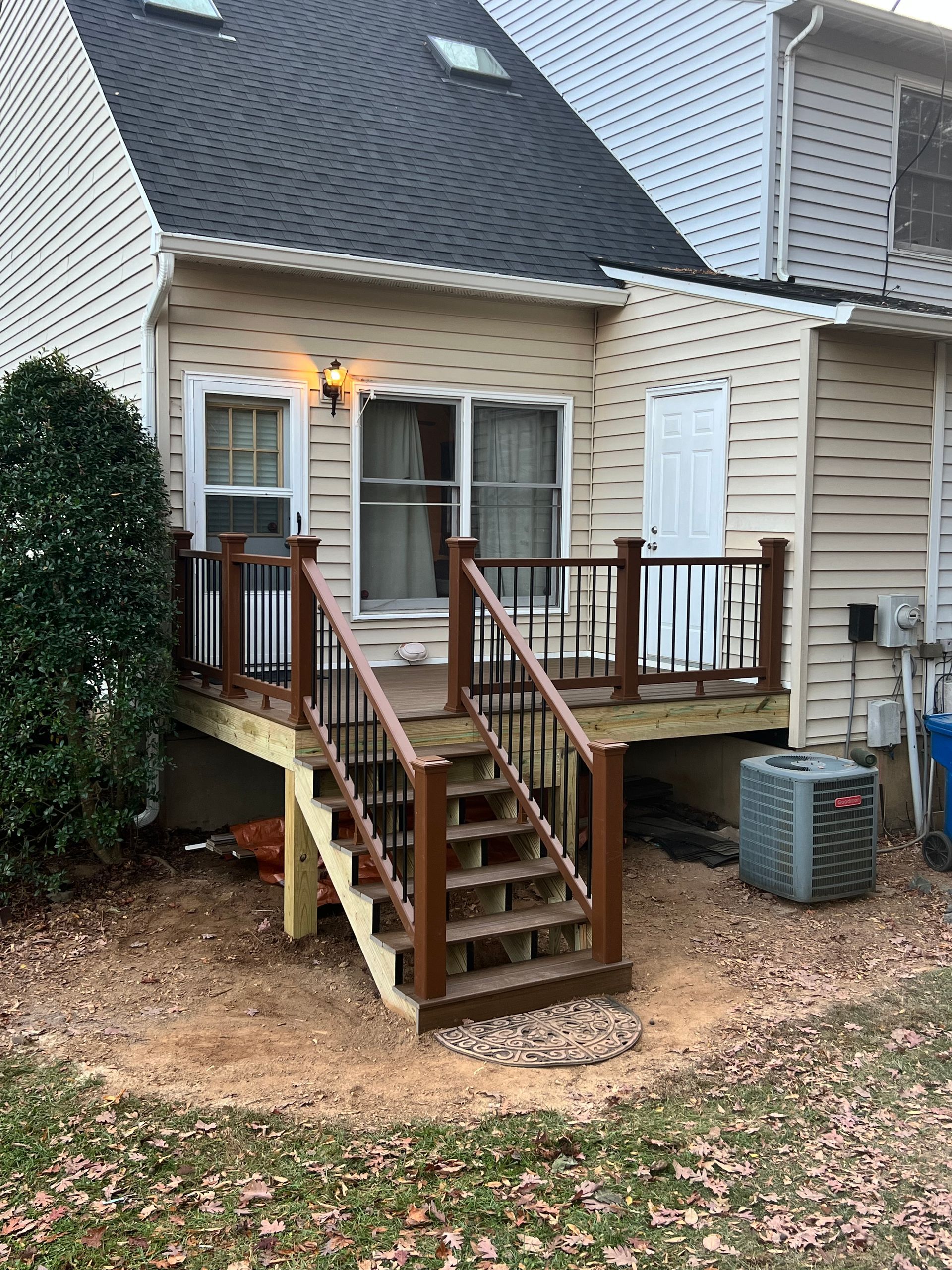 Deck with stairs leading up to a house. Brown stairs and railing, light tan siding.
