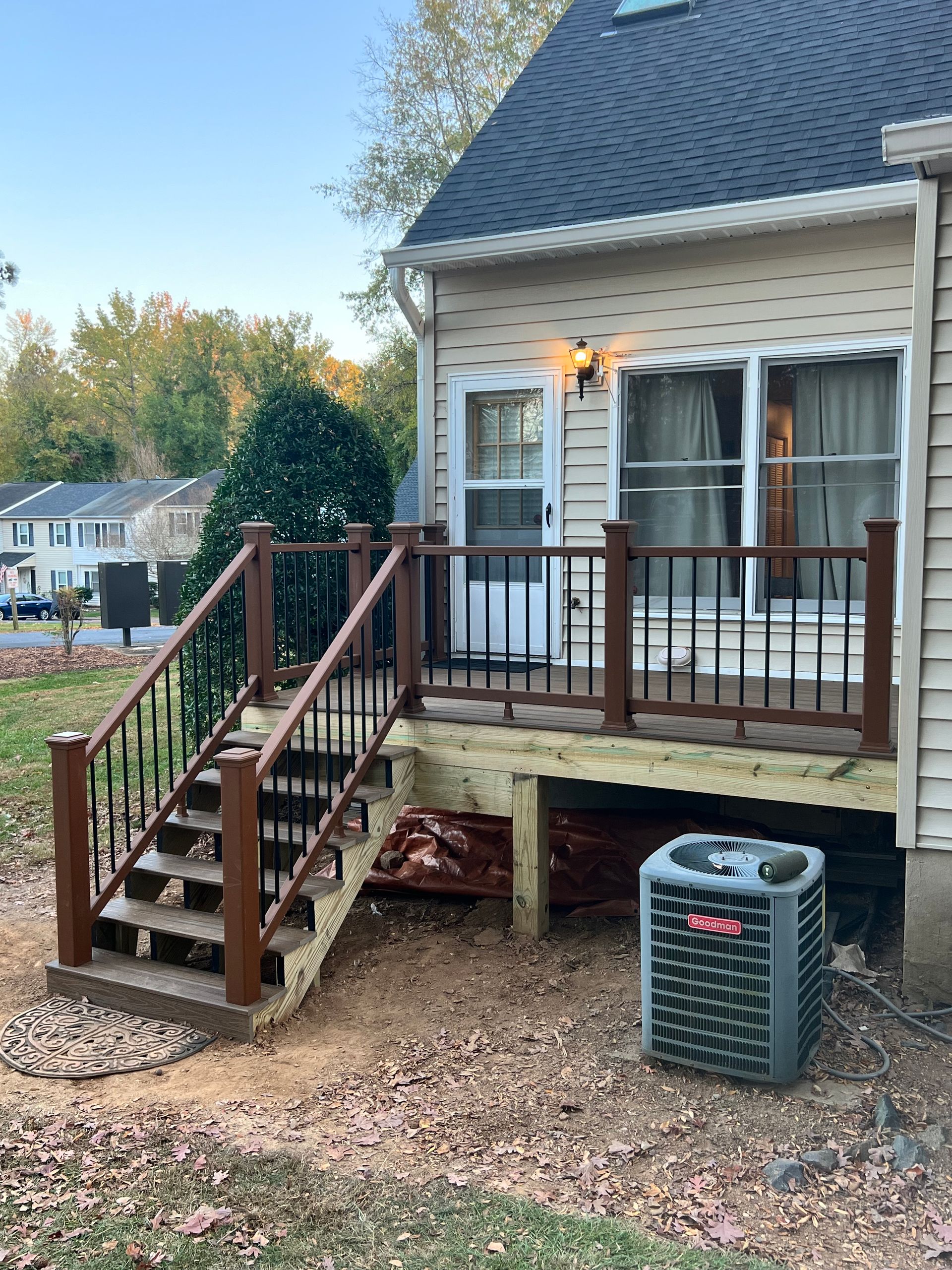 A wooden deck with stairs attached to a tan house; an AC unit sits below the deck.