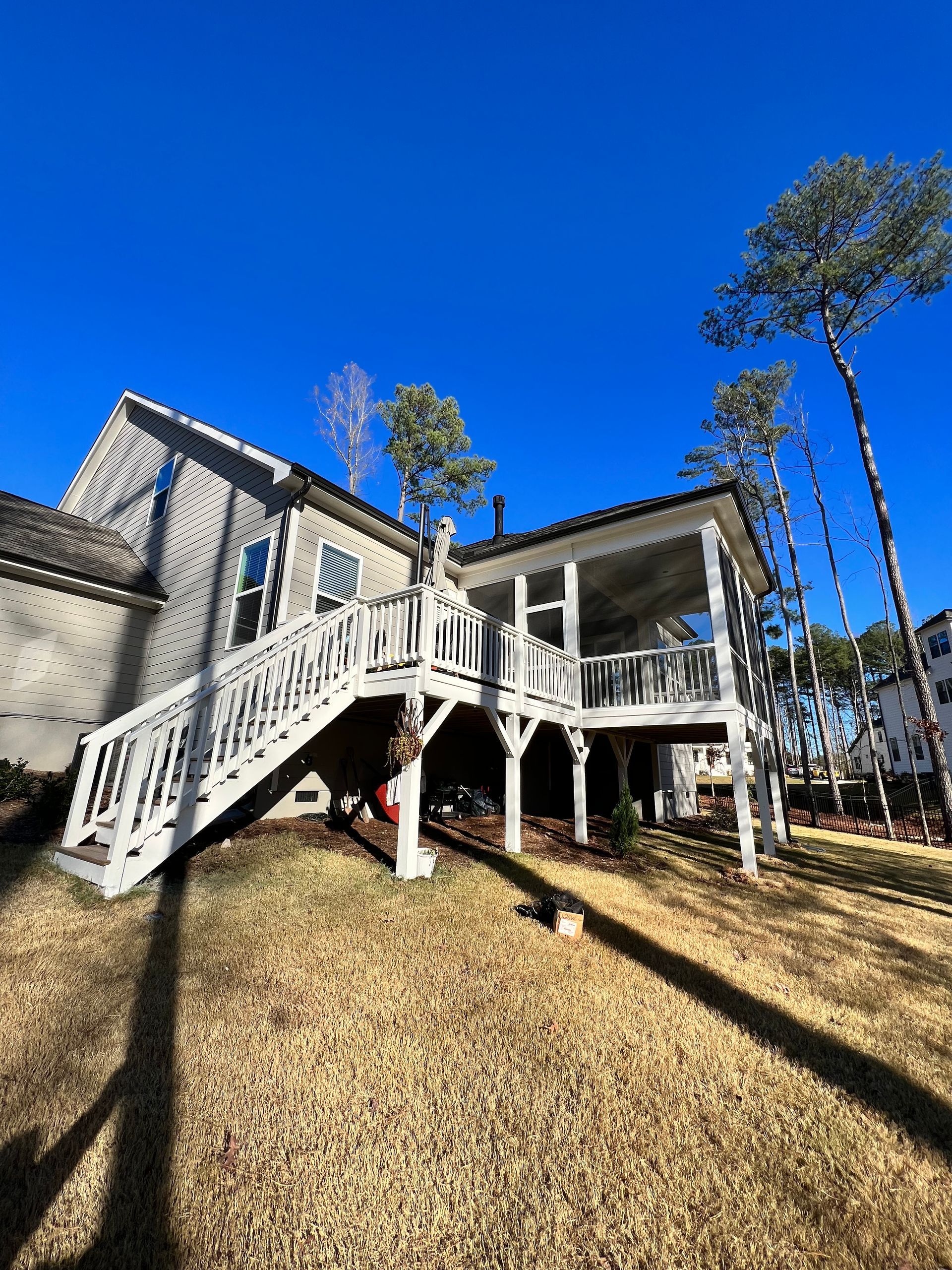 A two-story house with a white screened-in porch and staircase. Sunny day, blue sky.