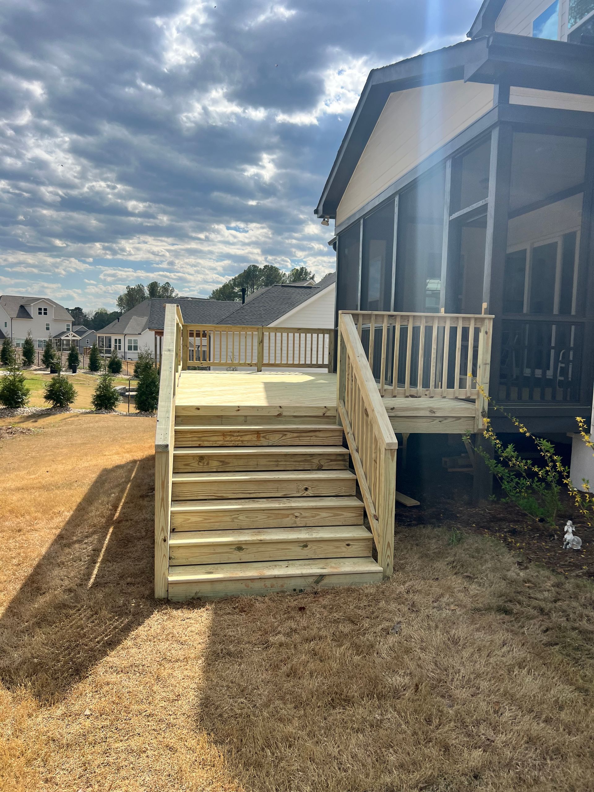 Wooden deck with stairs, built onto a house with a screened porch. Sunny outdoor setting.