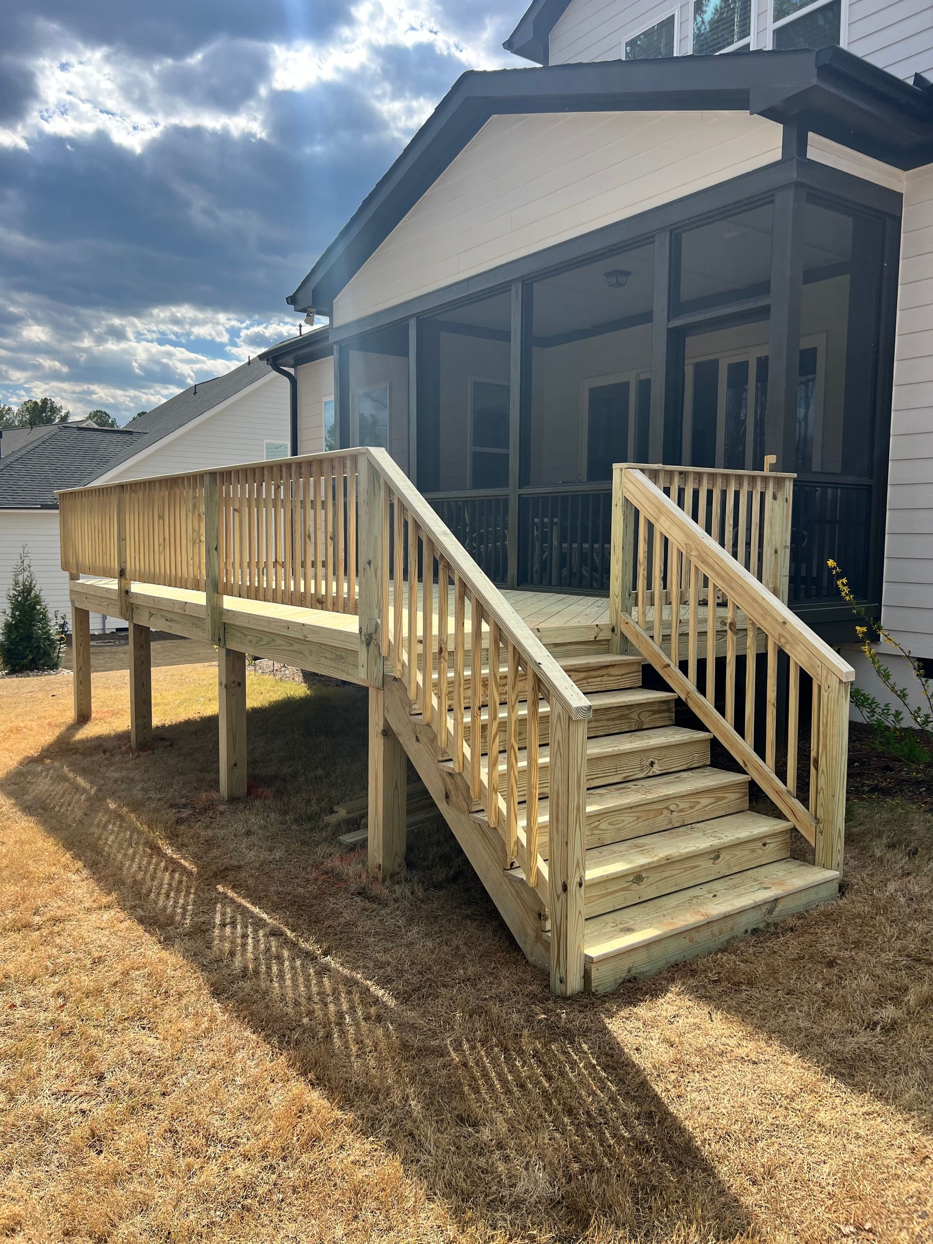 Wooden deck with stairs leading to a house, set in a yard under a cloudy sky.