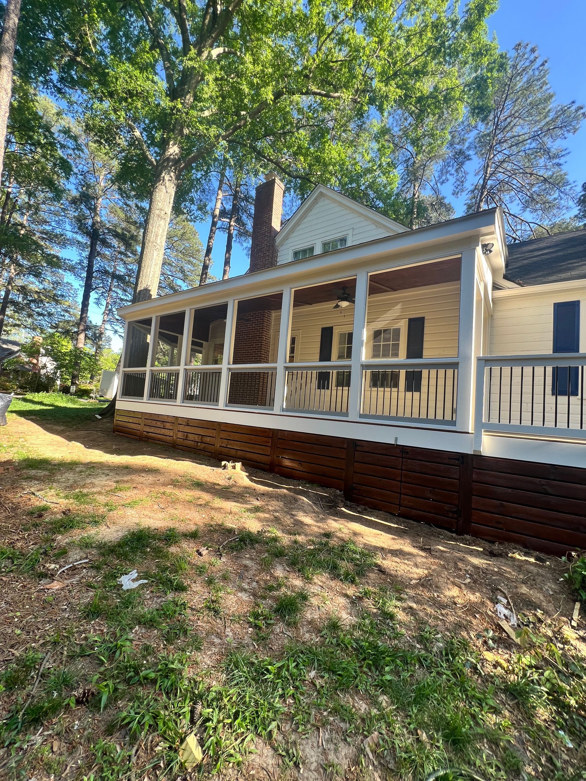 Yellow house with a screened porch and white railing in a backyard with trees.