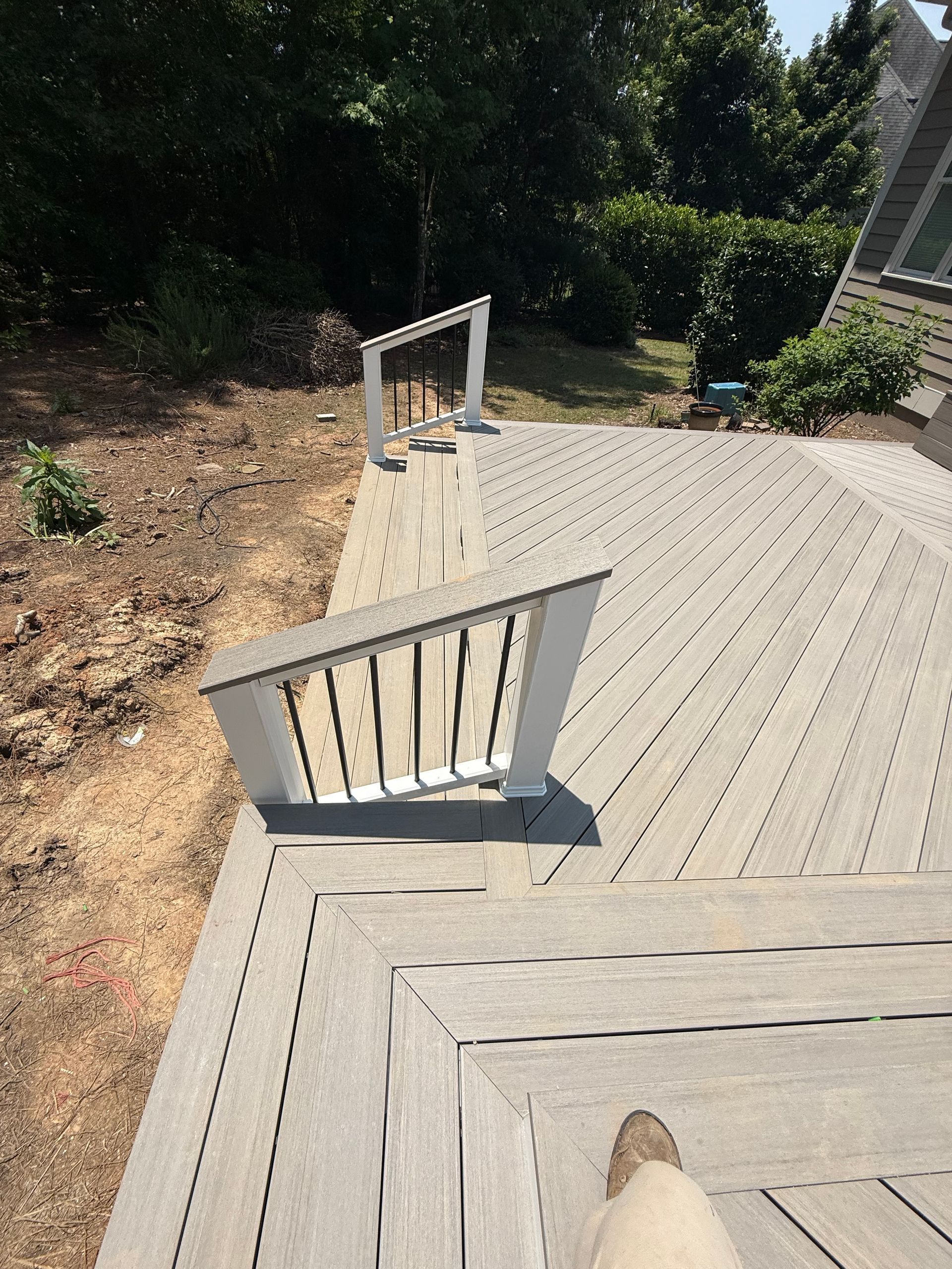 Grey composite deck with white railings. Person's foot visible. Outdoor setting.