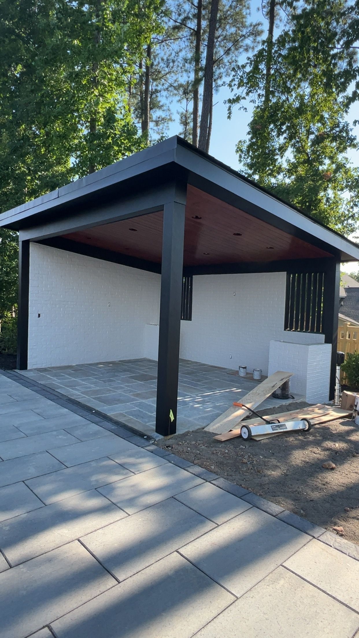 A modern gazebo with black trim and a red-brown underside, on a stone patio, with white walls.