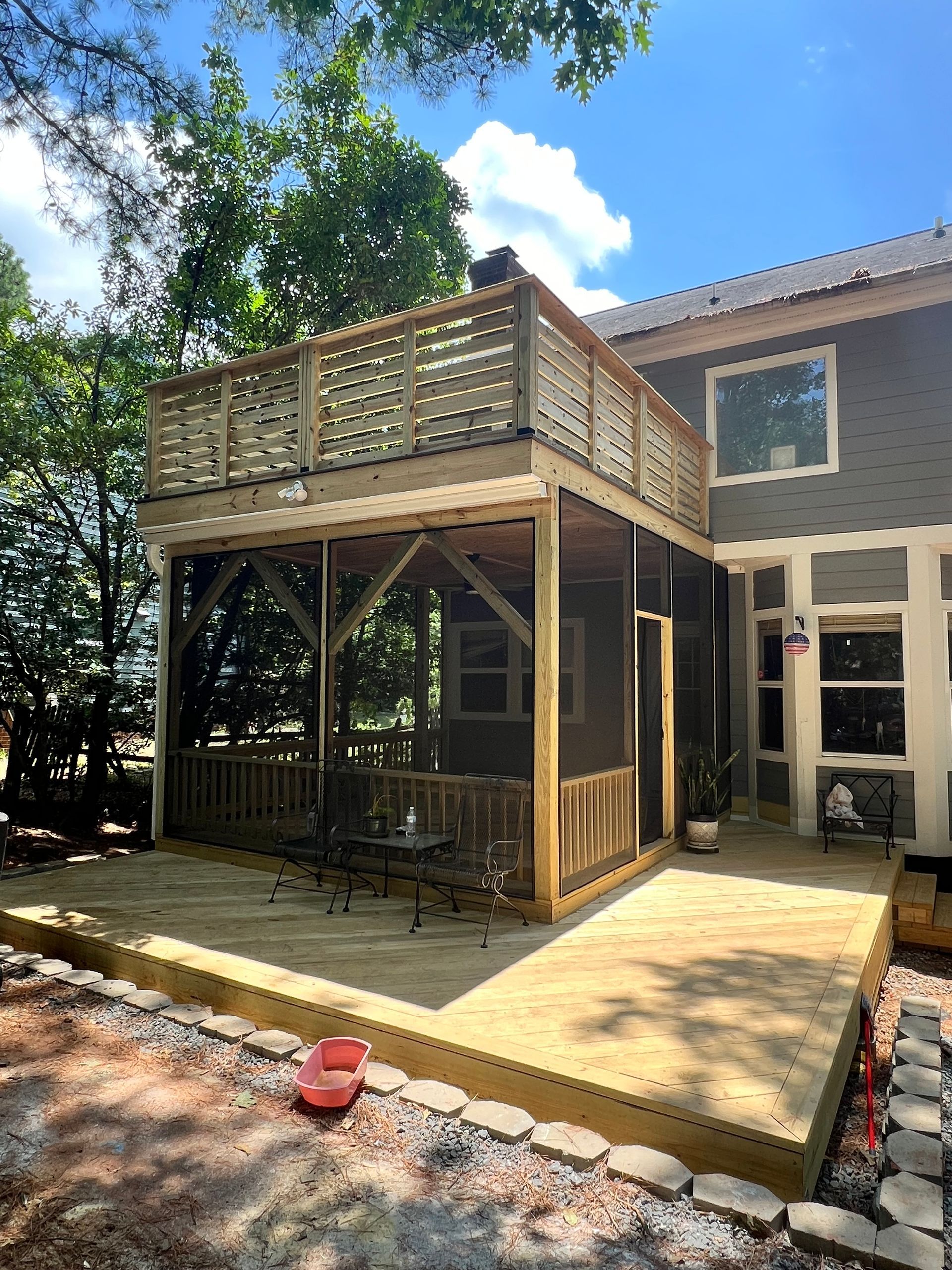 Wooden deck and screened porch attached to a house with a second-story deck, blue sky.