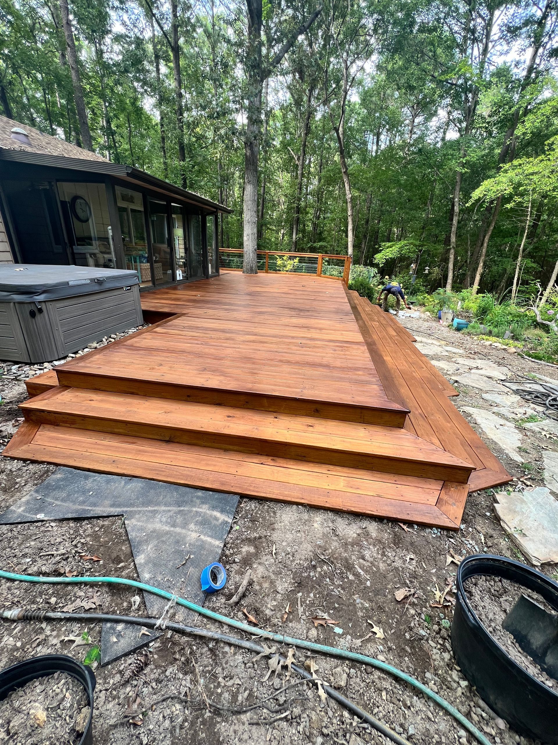 Wooden deck with steps in a backyard setting, next to a house with a hot tub.