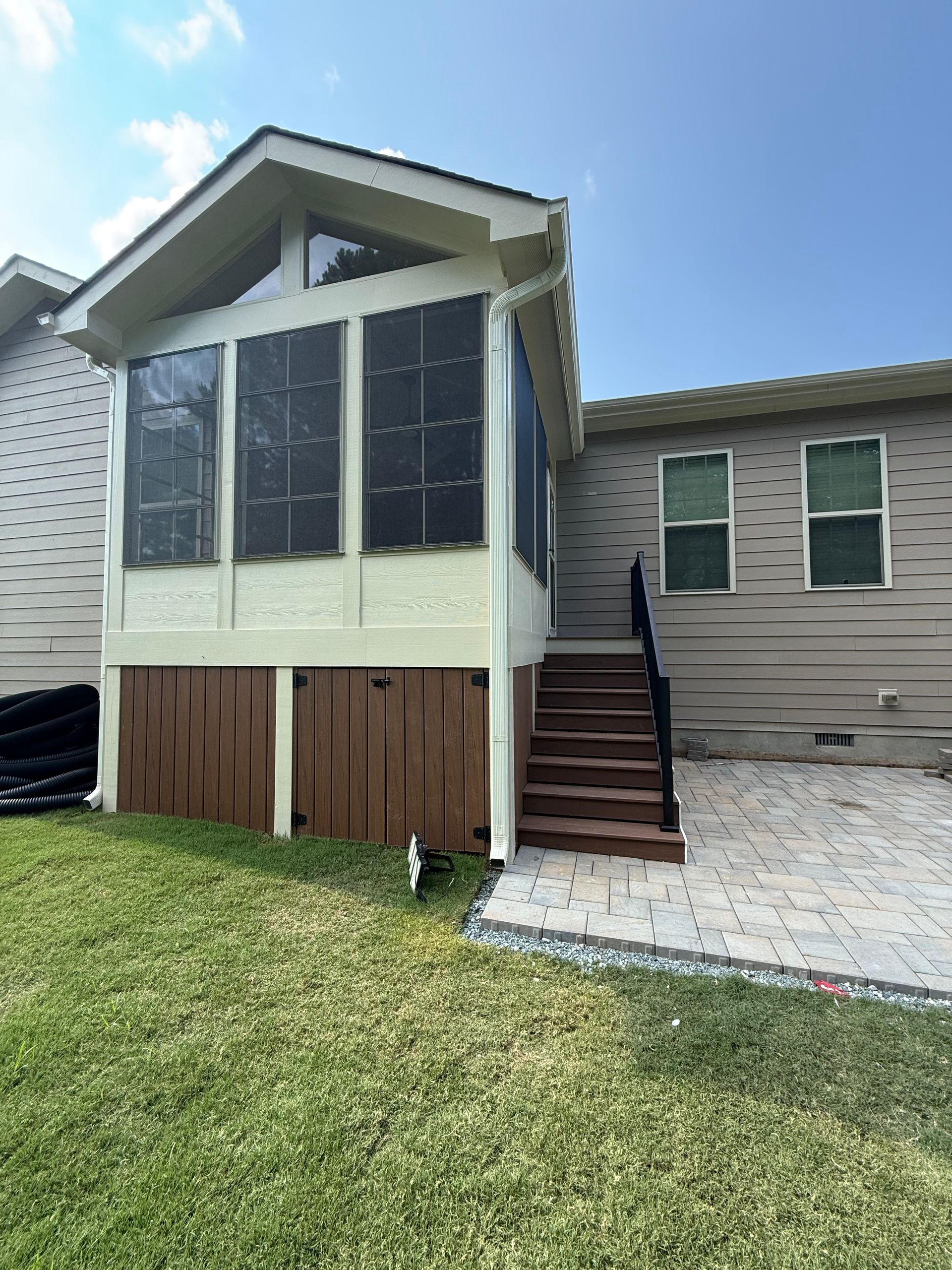 Screened-in porch with brown base, steps, and tan siding. Lawn and patio in the background.