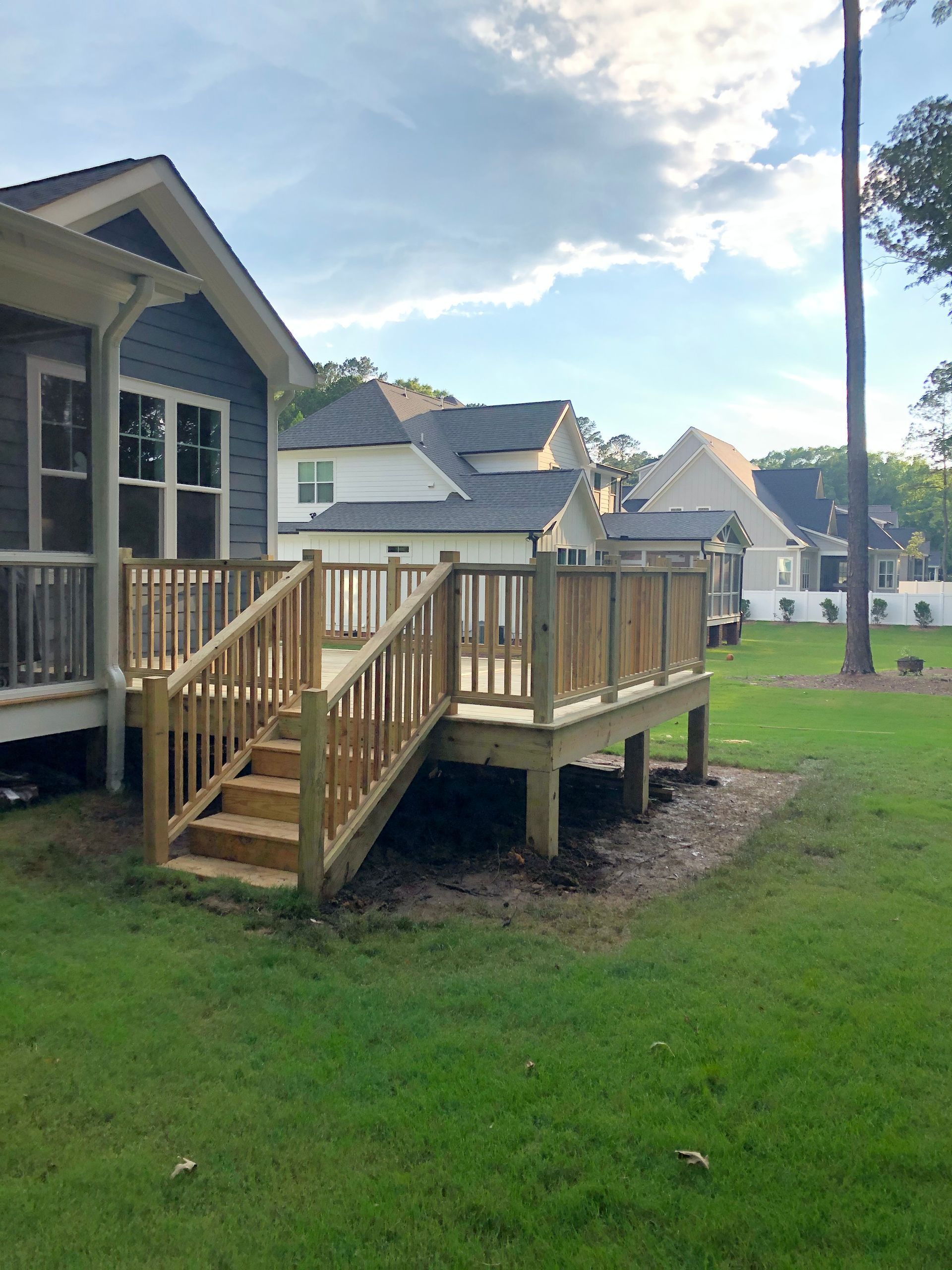 Wooden deck with stairs attached to a blue house; built in a grassy backyard.