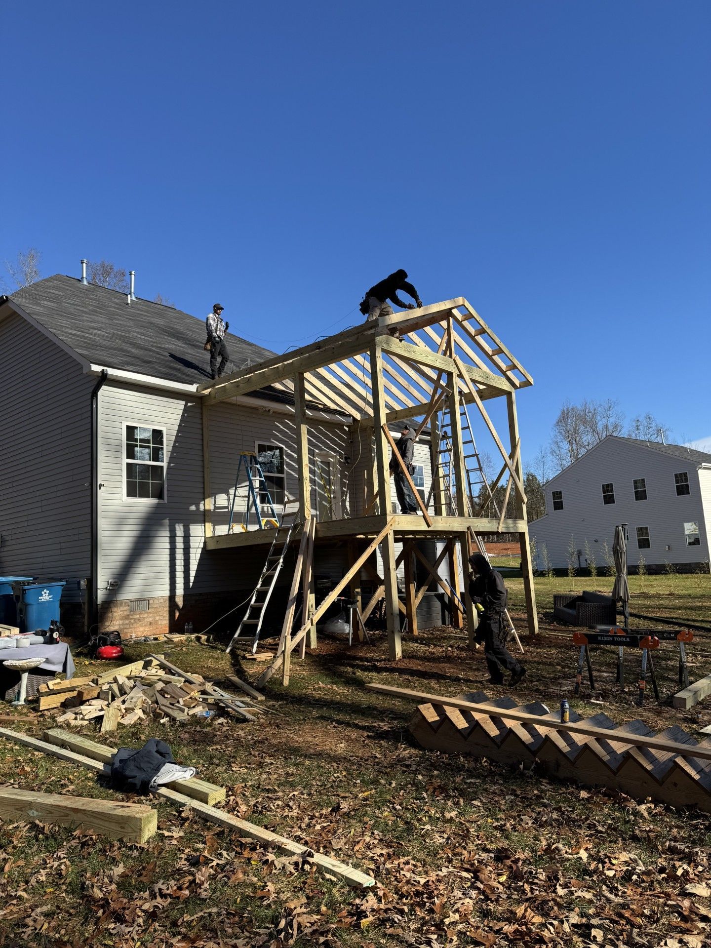 Construction workers building a wooden deck attached to a house sunny day.