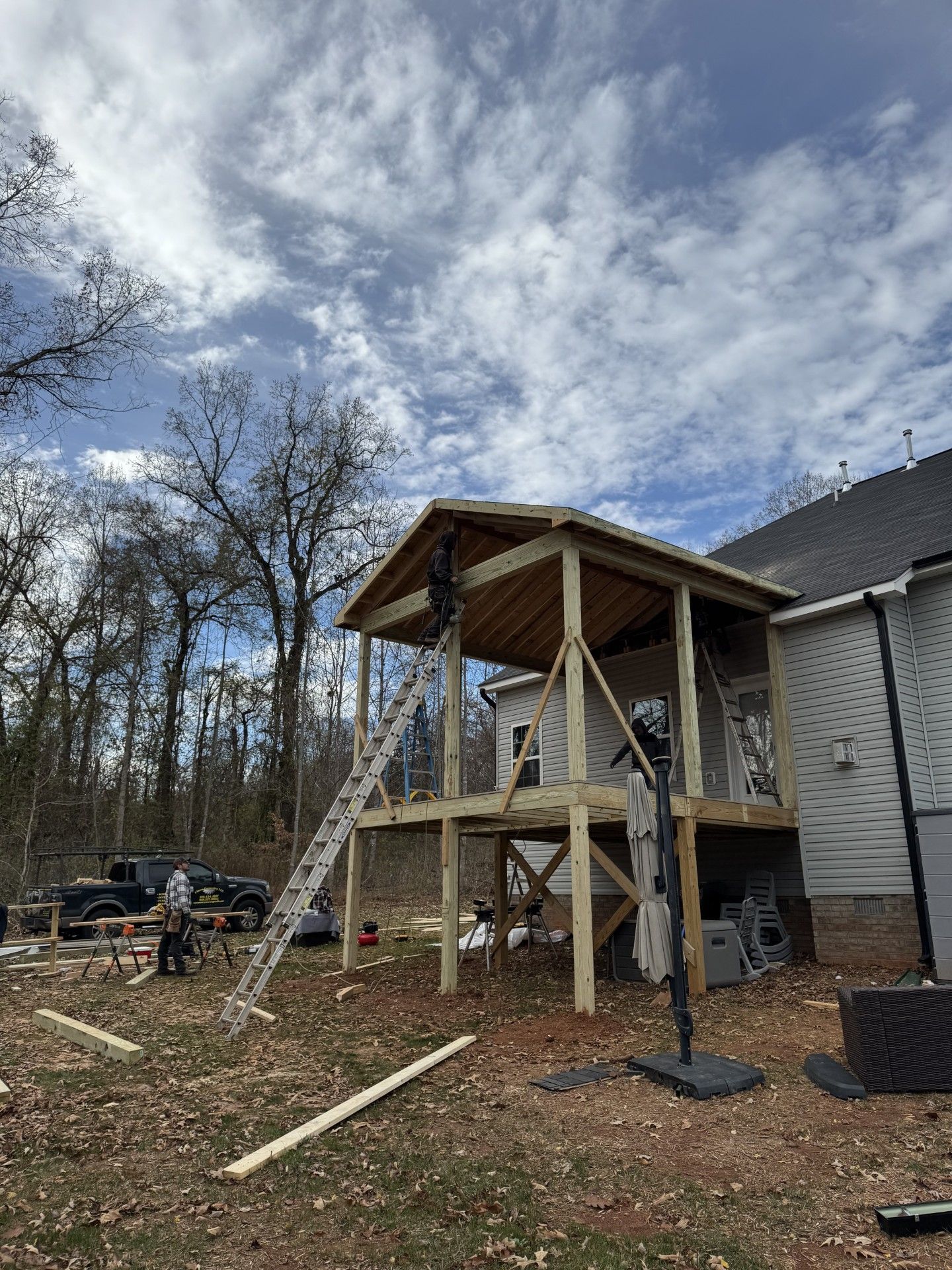 Construction of a two story wooden porch attached to a house workers, tools, and materials are visible outdoors.