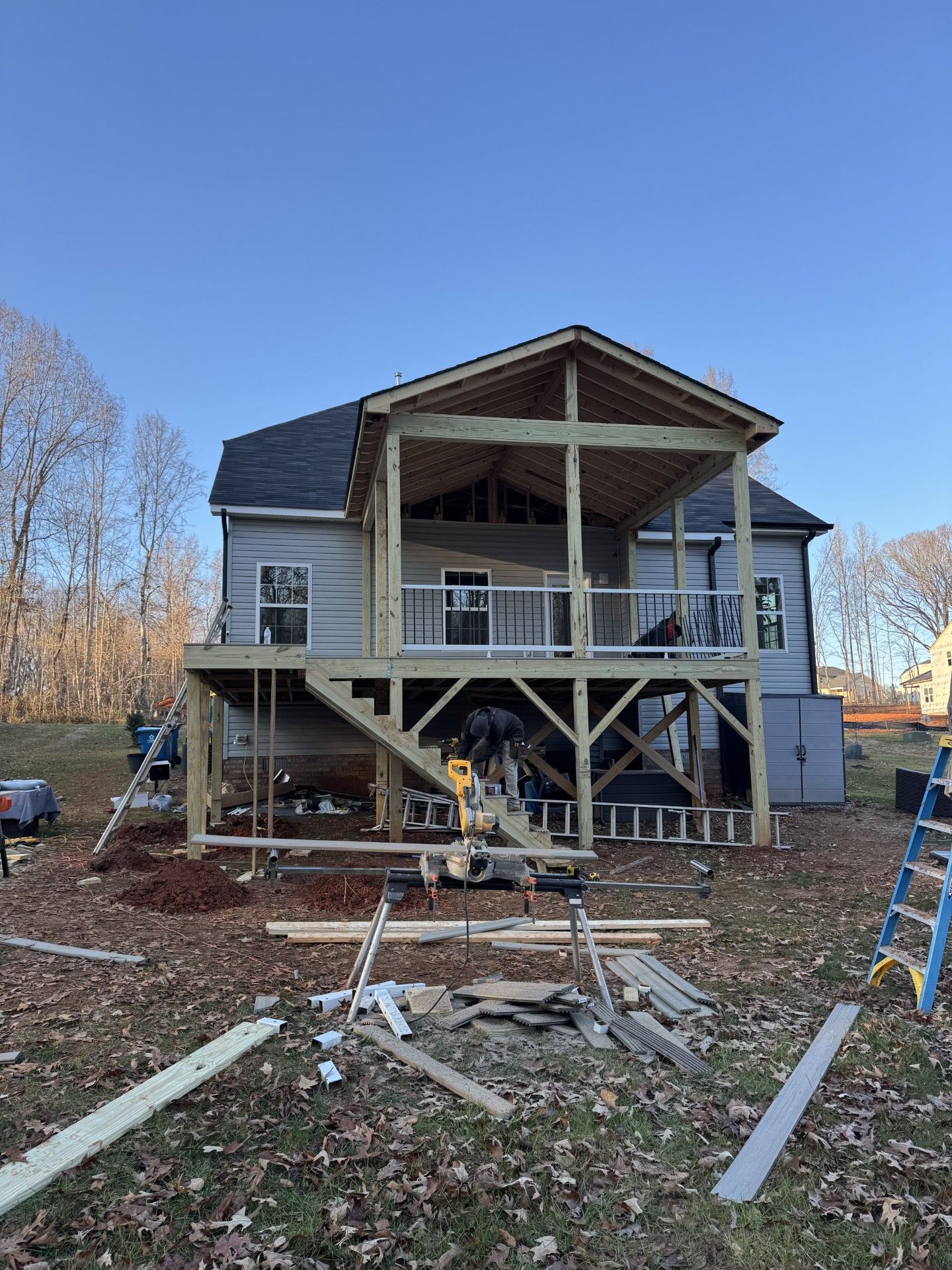 Deck construction in progress wooden frame with a covered porch attached to a gray house, set in a yard.