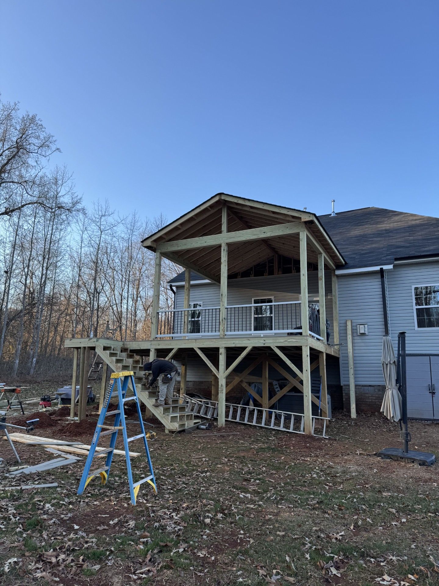 Wooden deck with attached roof under construction next to a house, with a person working on stairs.