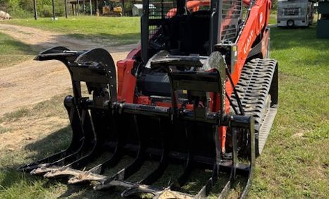 Orange skid steer with black grapple attachment on grass.