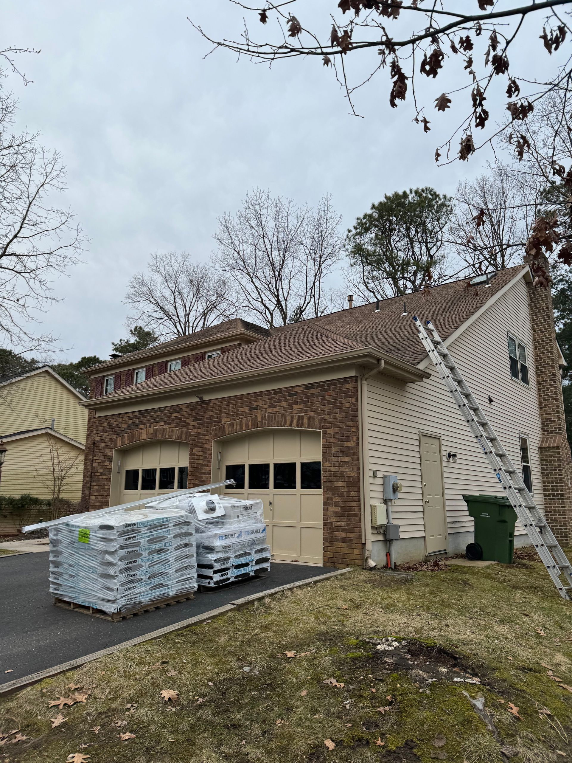 A house with a ladder in front of it and a stack of pallets in front of it.